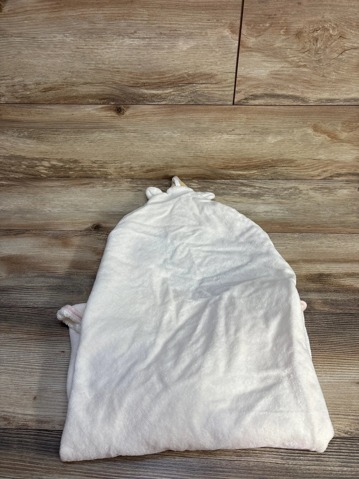 Flat lay of cream Cloud Island unicorn hooded baby towel showcasing hood with ears on wood flooring