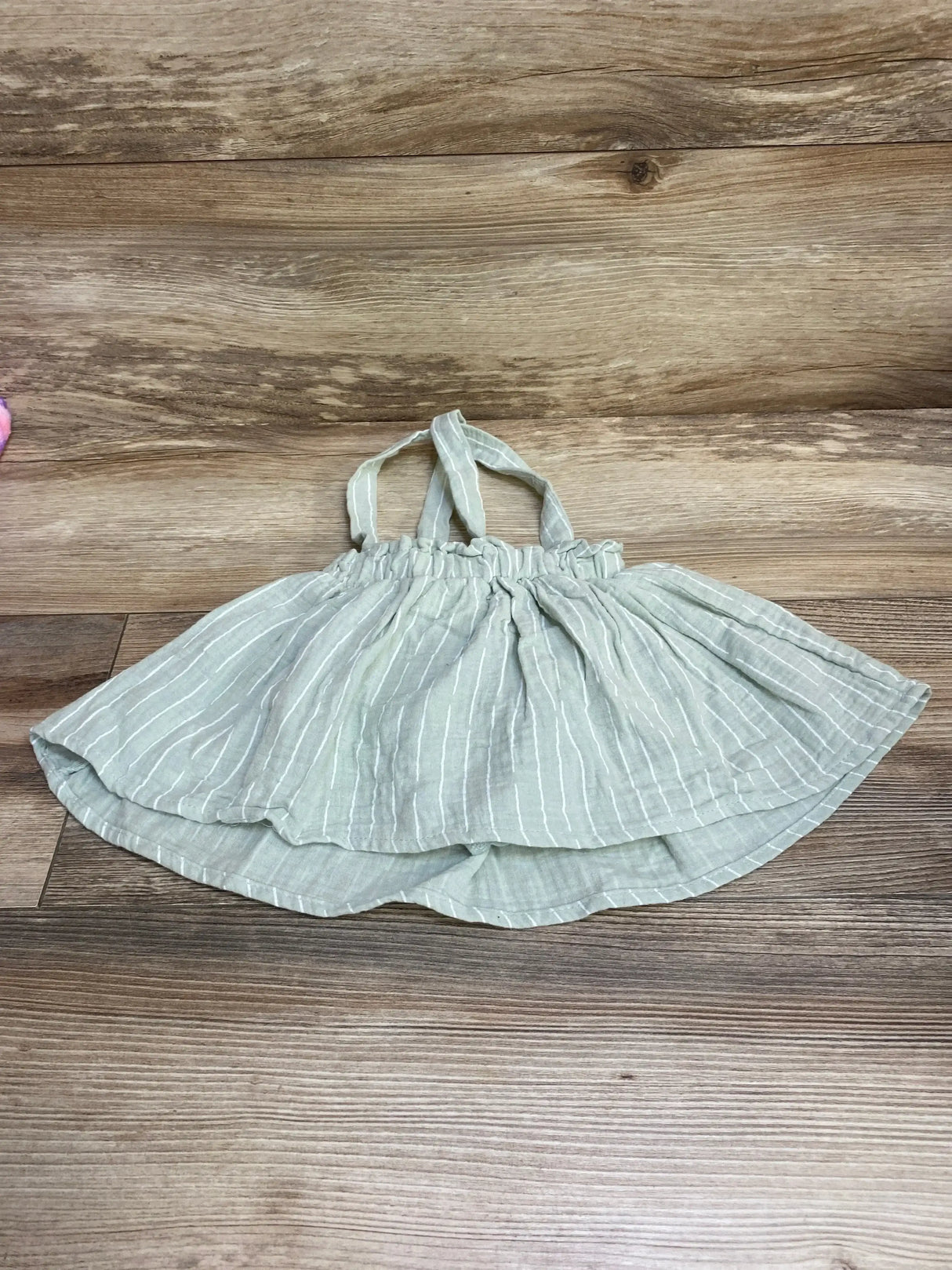Flat lay of green striped baby skirt and bloomers showcasing elastic ruched waistband and thin shoulder straps on wood background