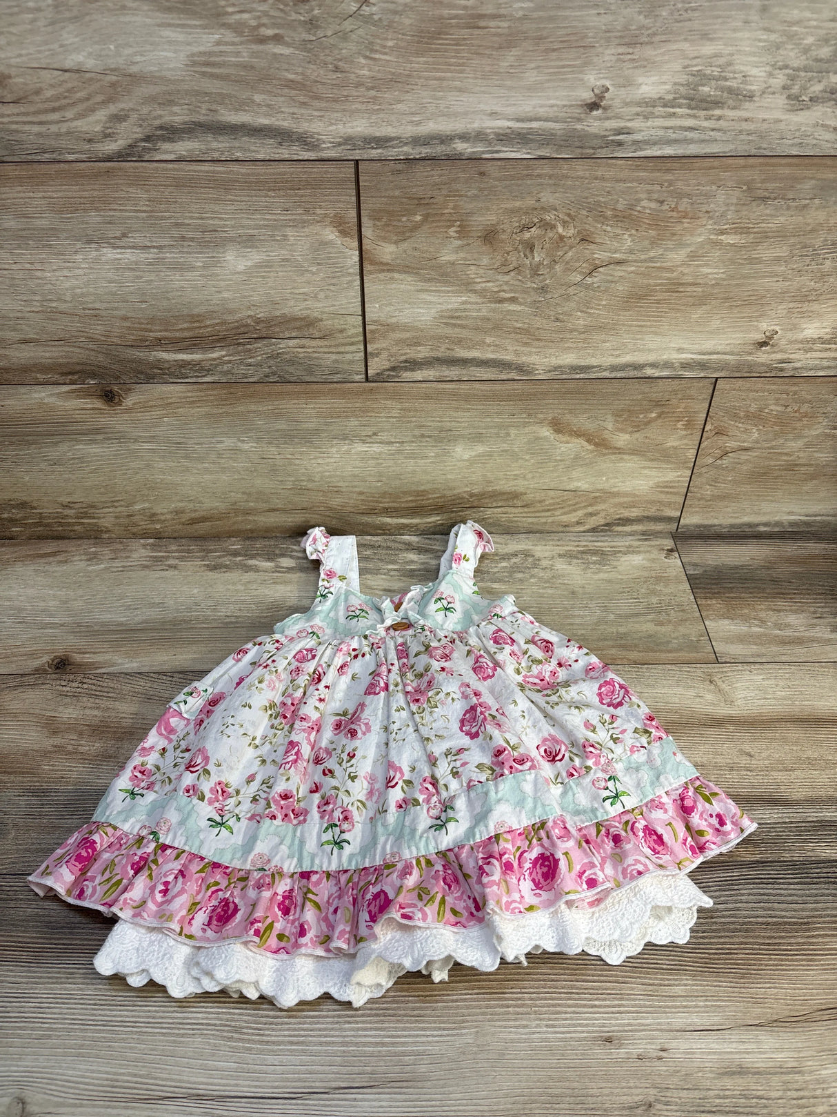 Top-down view of Sweet Honey sleeveless dress size 3T, white with pink rose print, ruffled hem and lace trim on wood floor