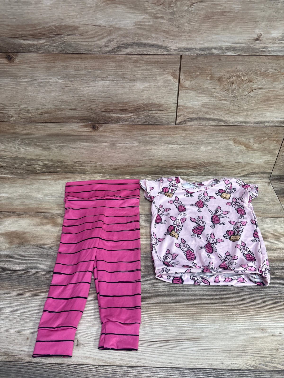 Flat lay of Disney Winnie the Pooh 2pc shirt and pants set showing pink striped pants and character-print shirt on wood