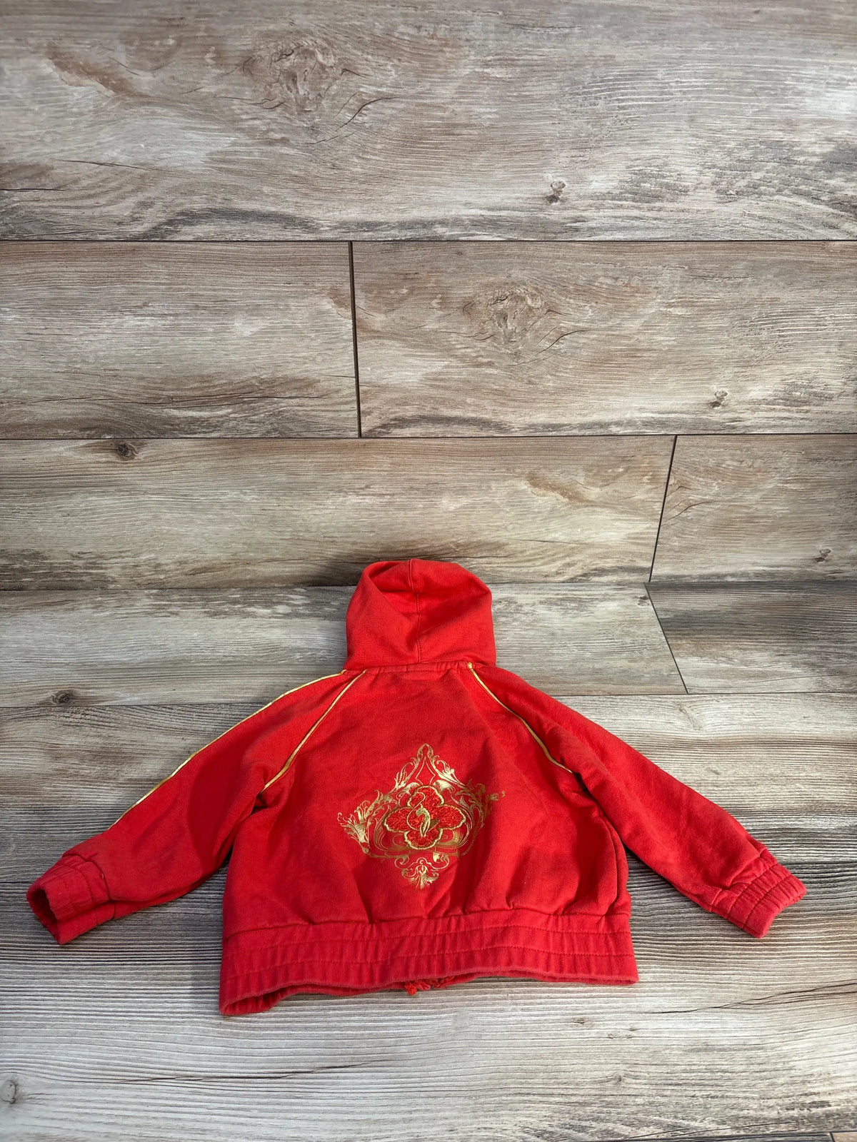 Back view of Baby Phat vintage zip-up hoodie showcasing gold back graphic with a wood-look floor background