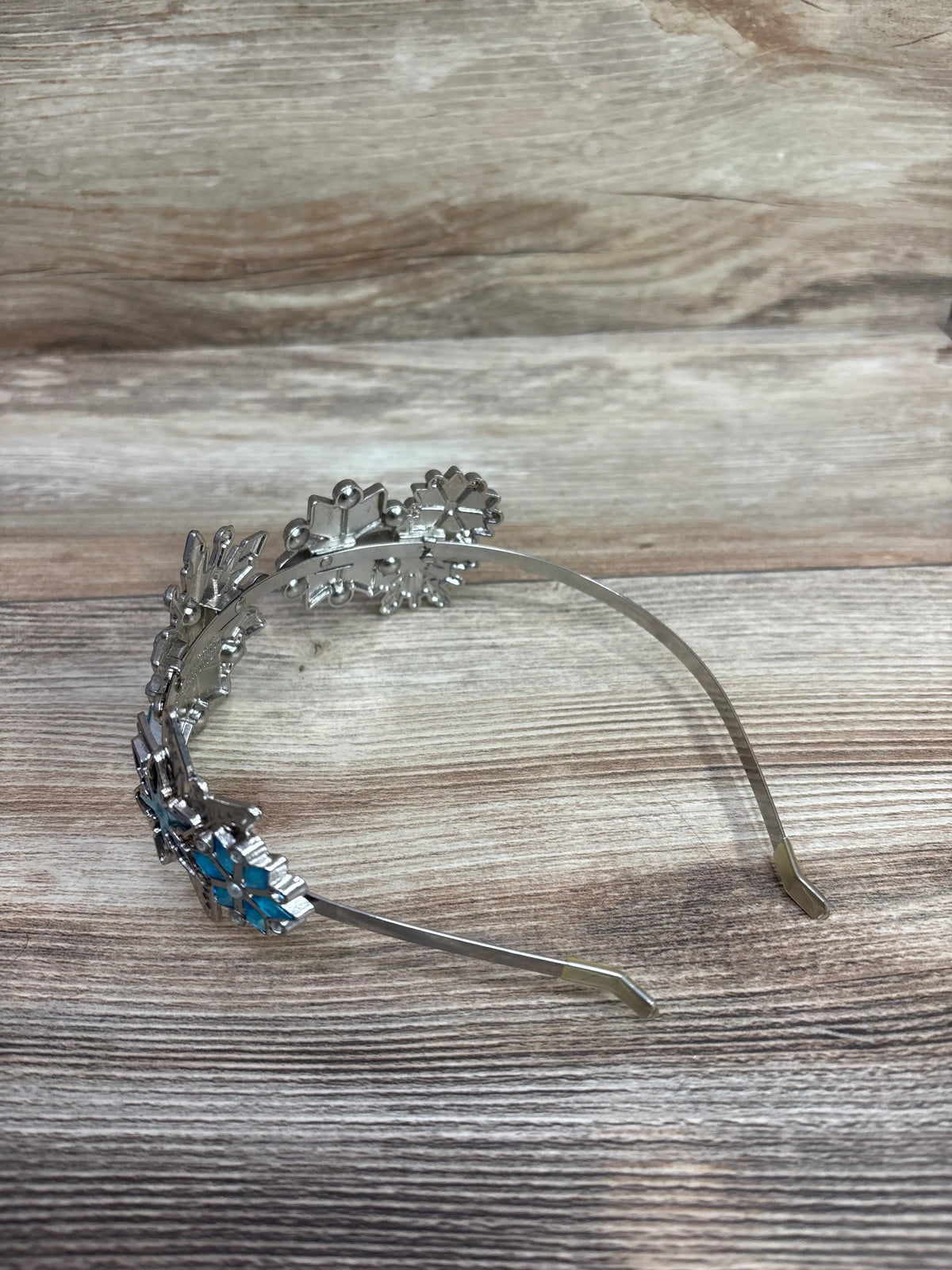 Angled view of Disney Store Frozen Elsa metal tiara headband showcasing blue jewel accents with a wood-grain background