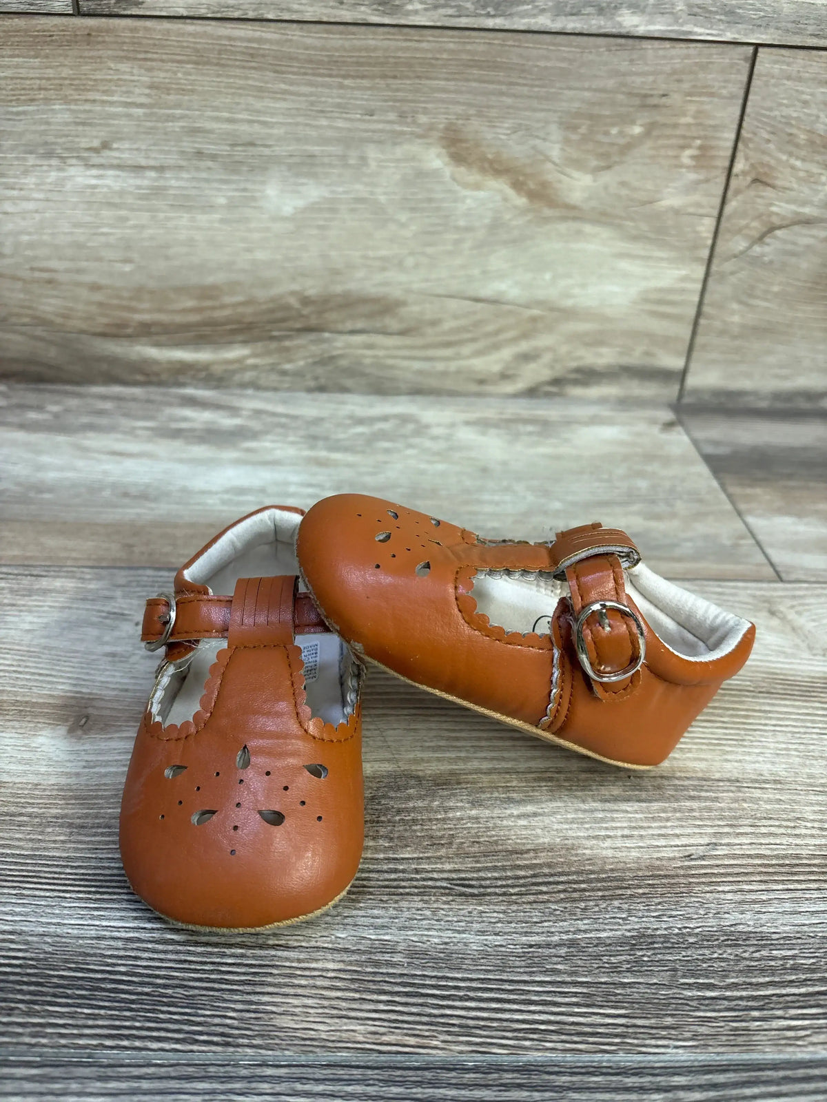Front and side view of Sienna chestnut baby sandals showcasing scalloped edges, floral cutouts, and buckle on wood background