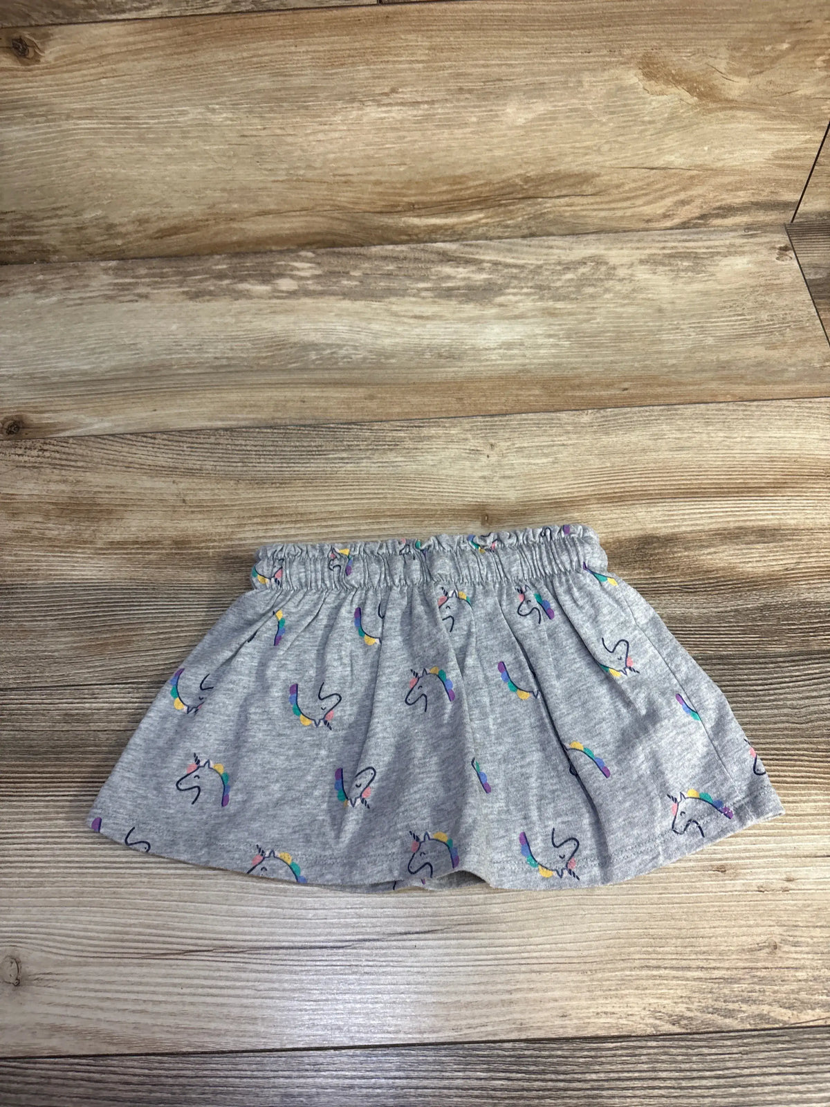 Front view of Cat & Jack gray drawstring skort with colorful unicorn print and elastic waist on a wood floor