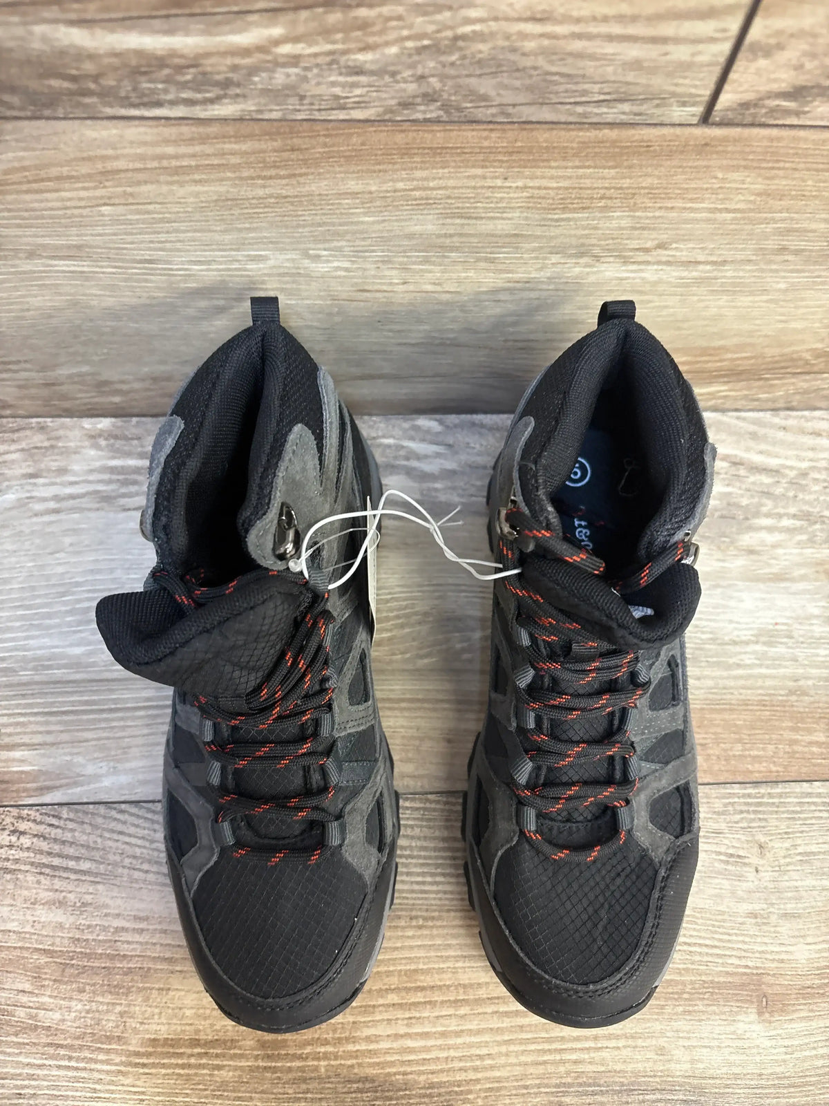 Pair of black and gray kids hiking boots with red laces on wooden floor
