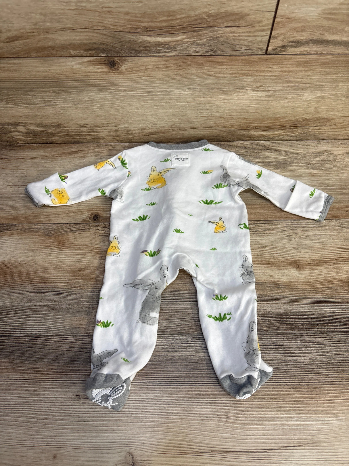 White baby sleeper with bunny and chick print on wood floor, footed pajamas
