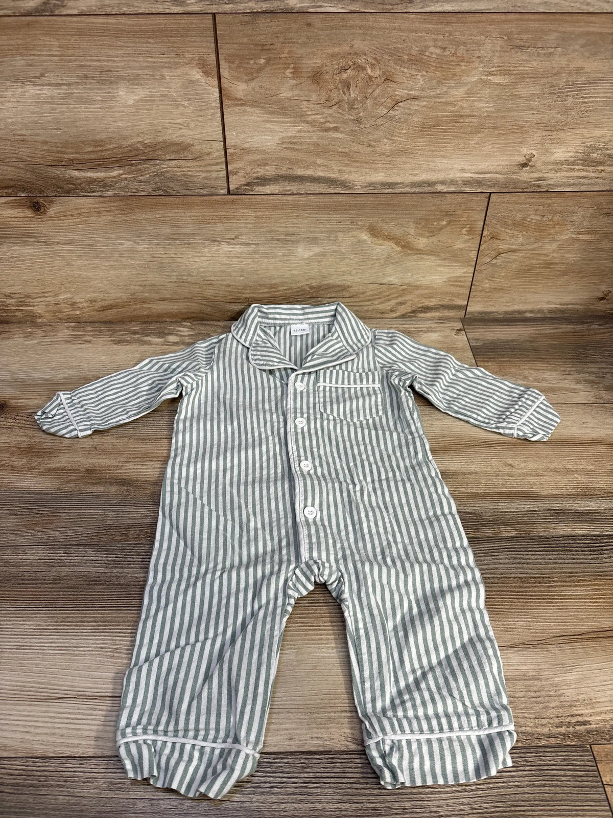 Front view of a green-and-white striped button-up coverall with long sleeves, chest pocket, and footed legs on wood