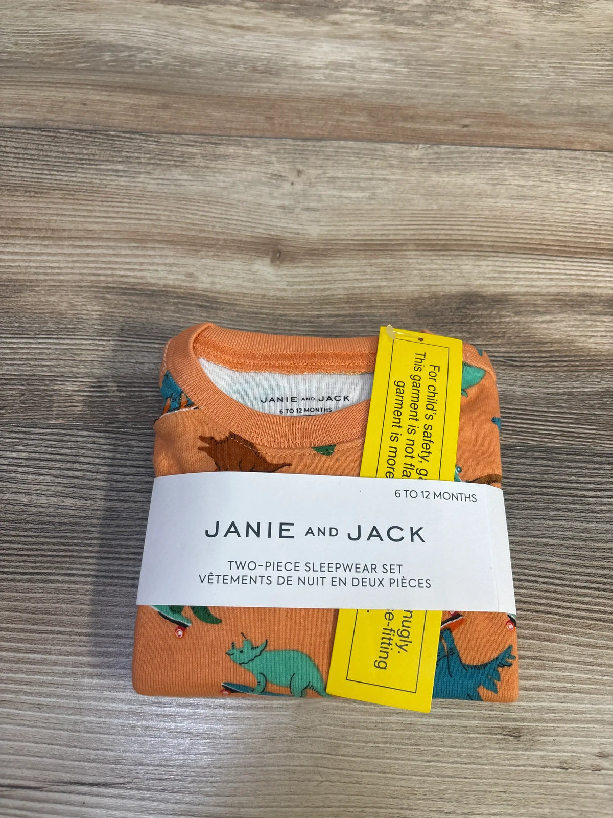Top view of NEW Janie & Jack Dino Skate 2pc Pajama Set Orange sz 6-12m folded in original Janie and Jack sleepwear band on wood plank background