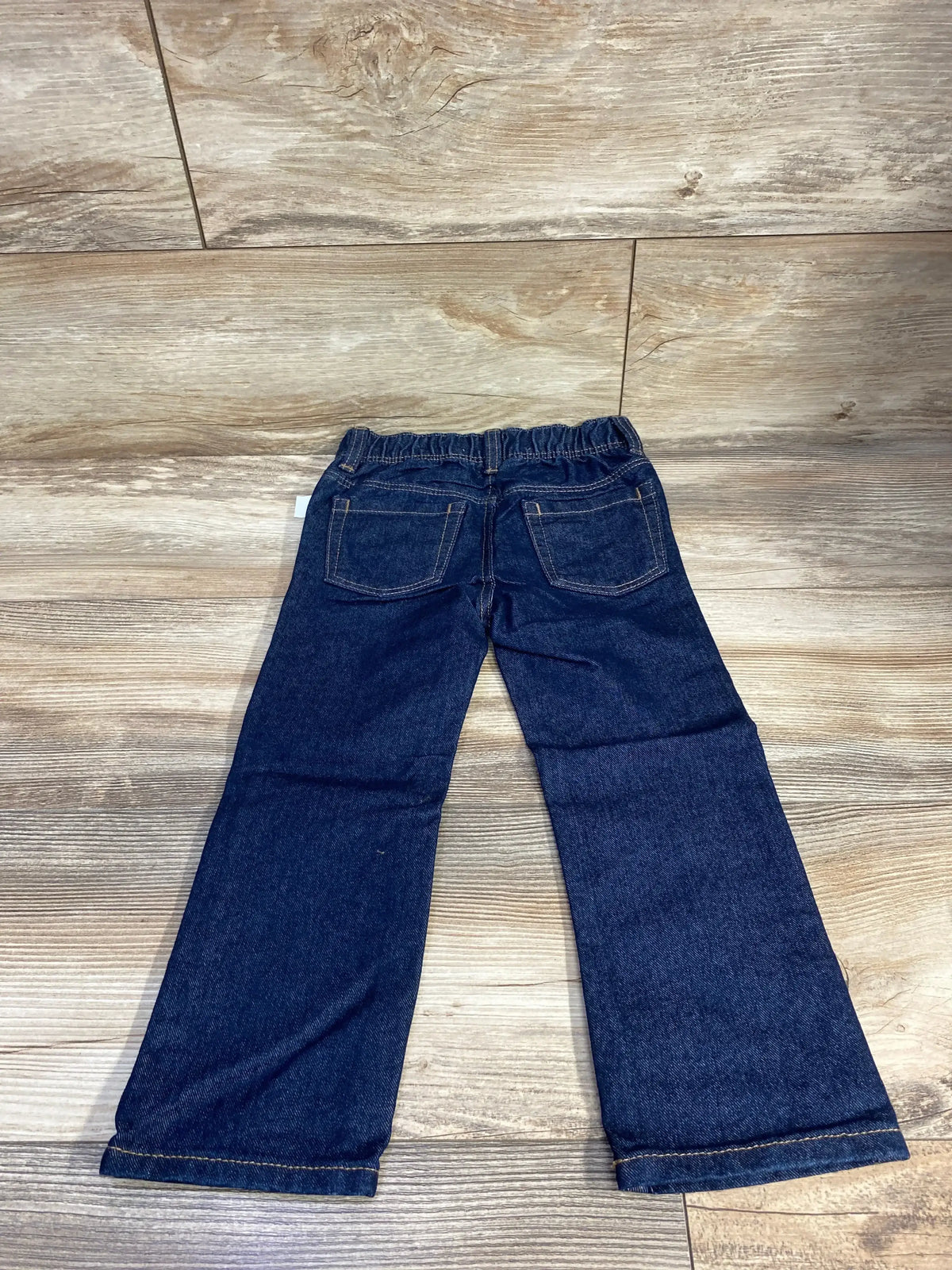 Dark blue kids denim jeans with elastic waistband, back pockets, laid flat on wood floor