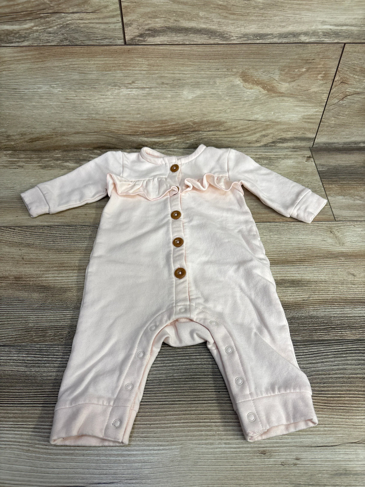 Light pink baby romper with ruffle detail, front buttons and snap closures on wood floor