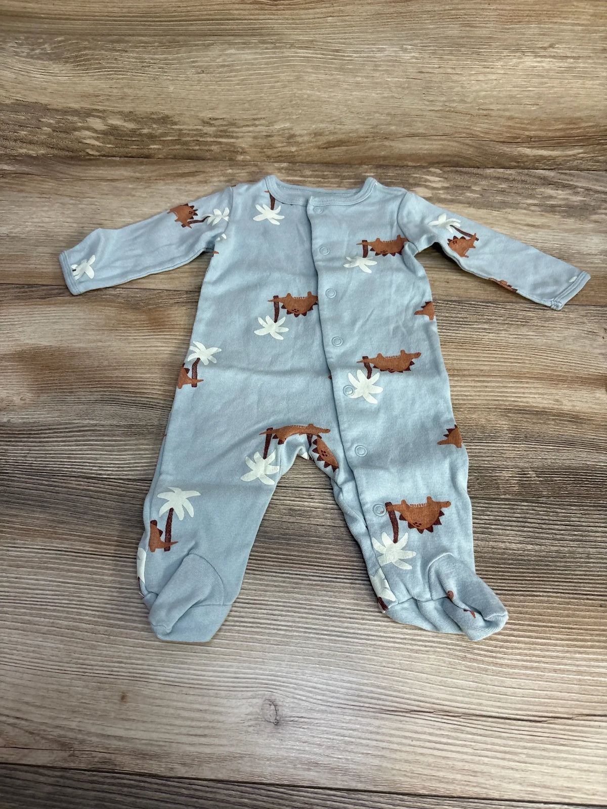 Flat lay of Carter’s footed sleeper in light blue with brown dinosaur and white palm tree print on wood plank floor