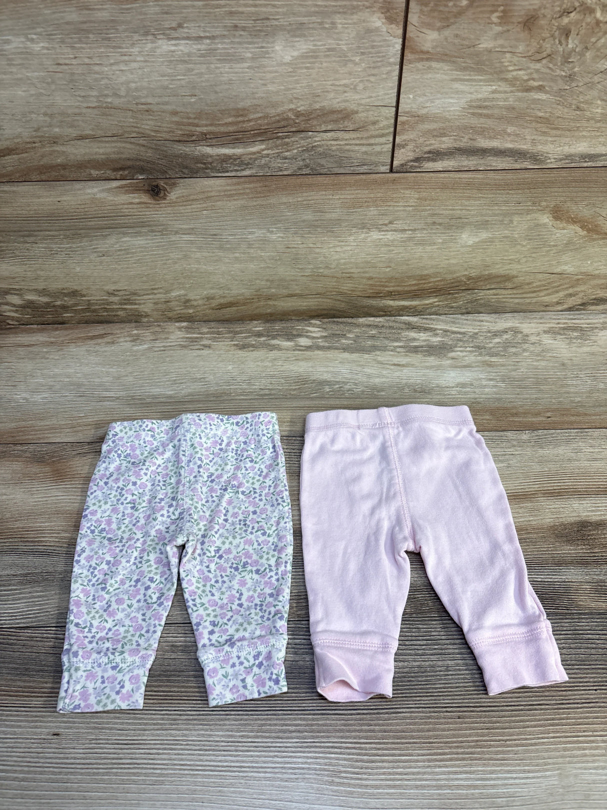 Flat lay of two 3M baby pants: solid light pink and white with pink floral print, cuffed ankles on wood background