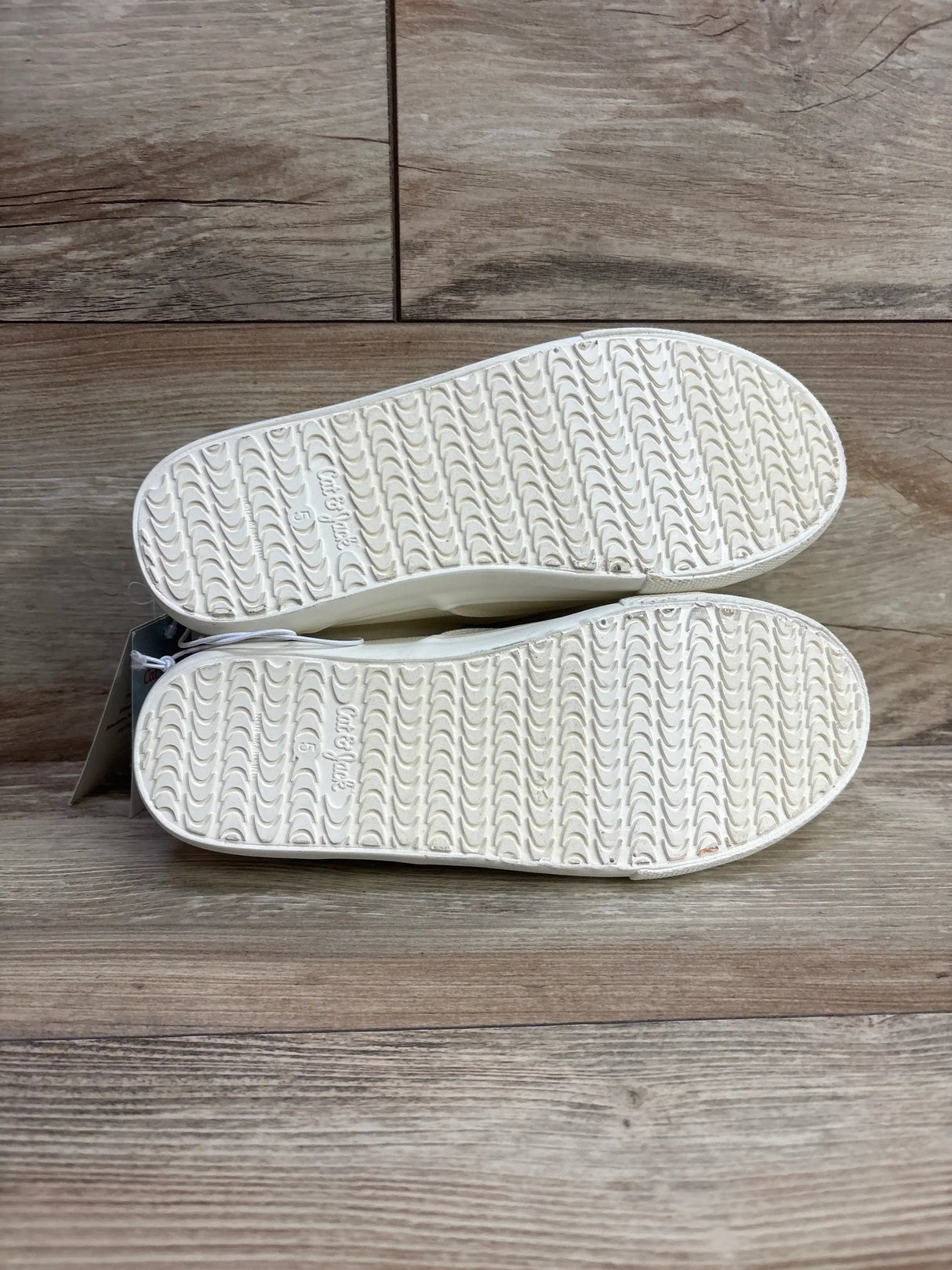 Bottom view of NEW Cat and Jack Tyler Slip-On Sneakers in off-white sz 5Y showcasing unworn cream textured grip soles with hangtag on wood plank floor