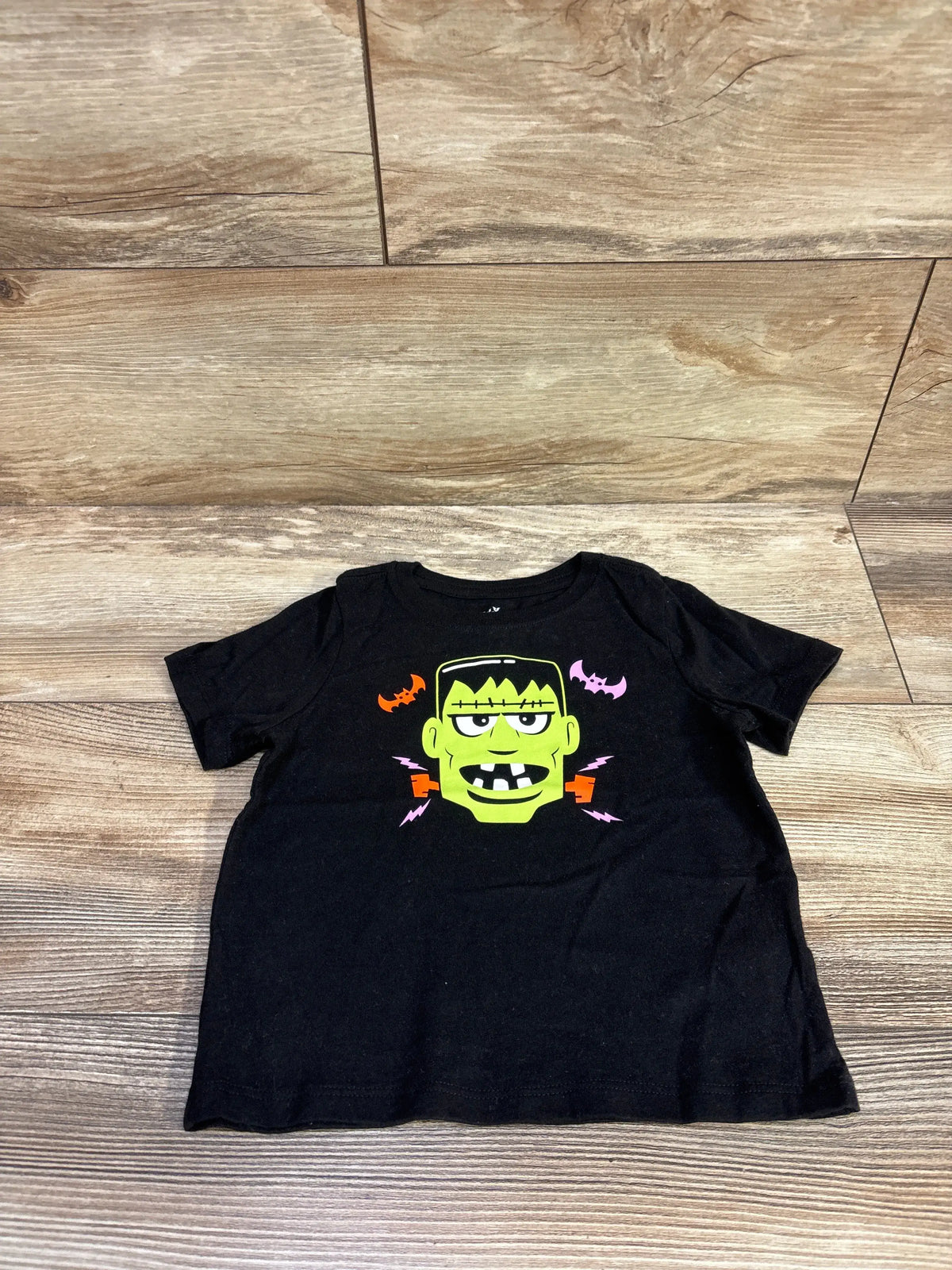 Front view of a black Halloween Frankenstein shirt showcasing a colorful Frankenstein graphic on a wood floor