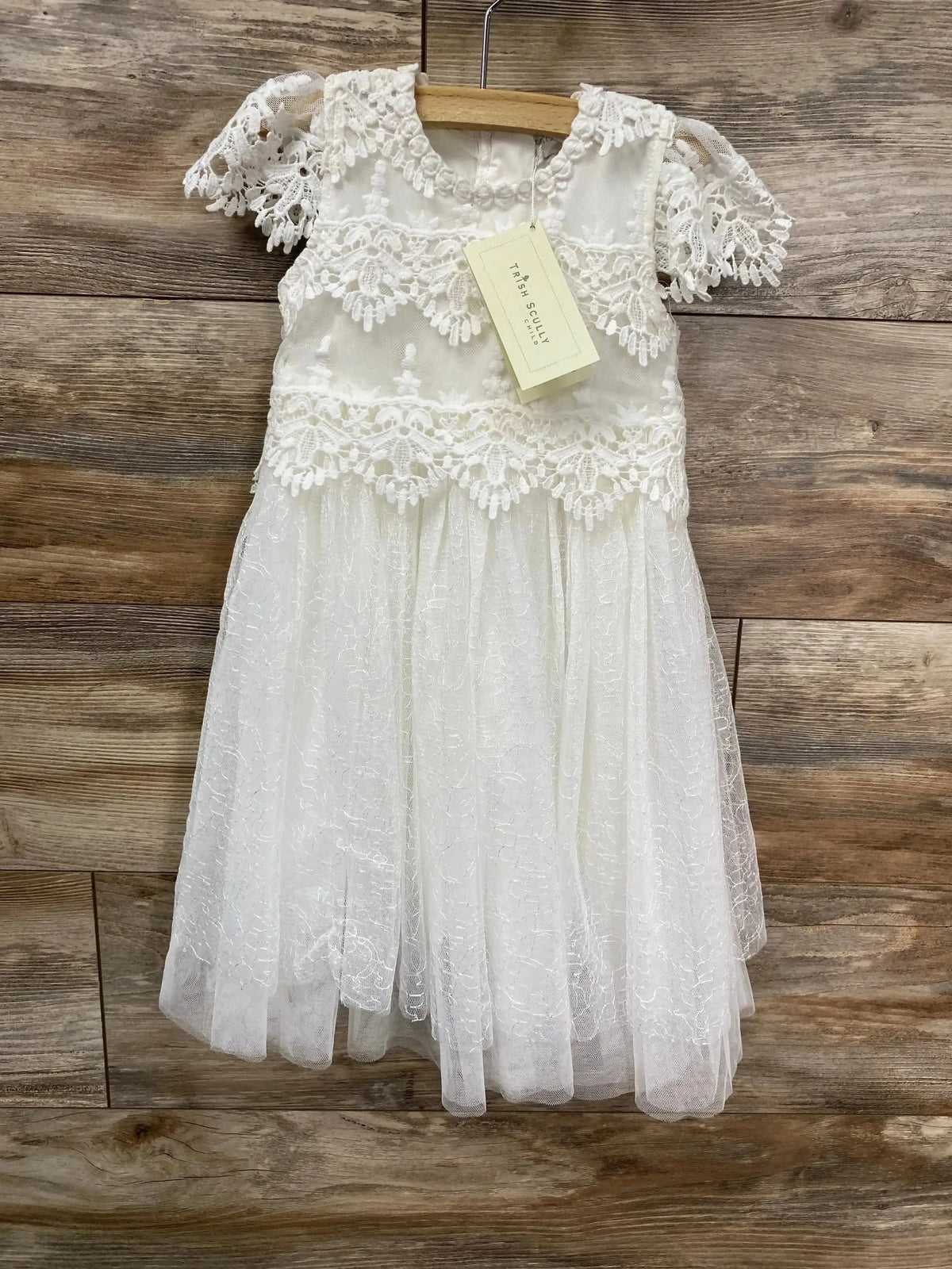 Front view of Trish Scully white lace toddler dress size 2T showing scalloped bodice and flutter sleeves on wood background