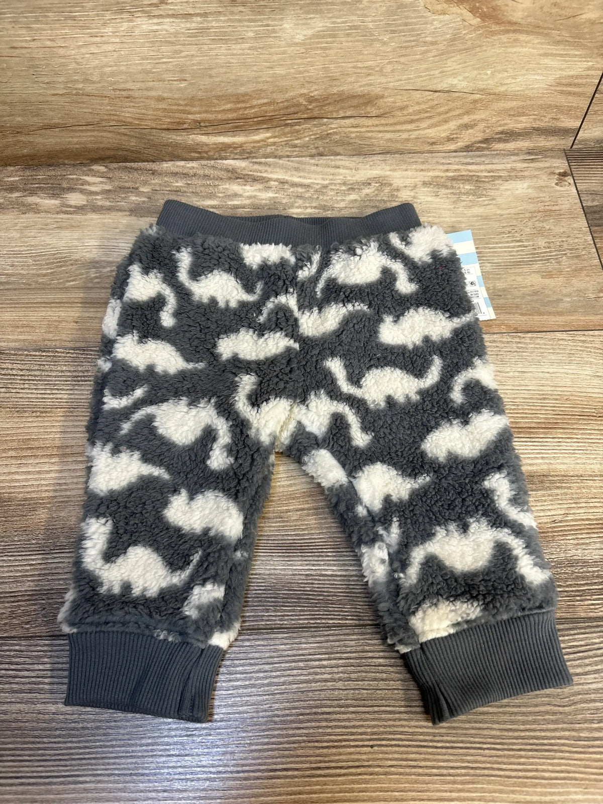 Grey fleece baby pants with white dinosaur print on wood floor background