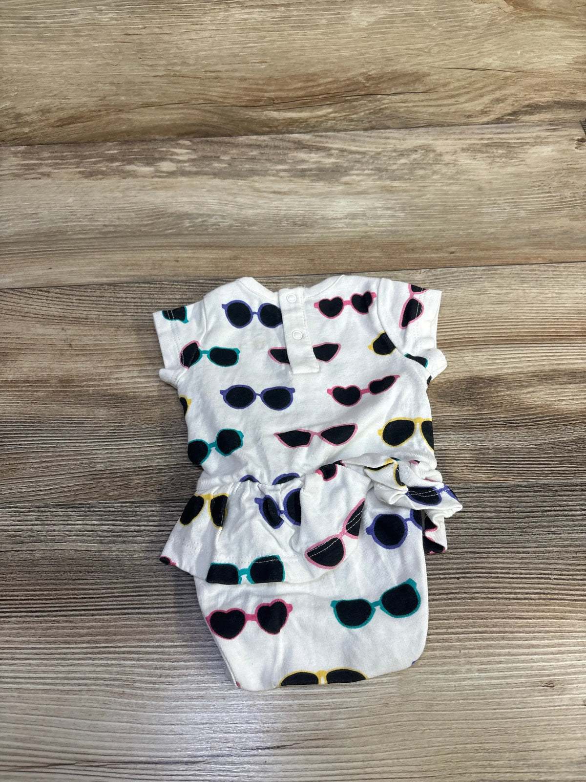 Front view of white skirted bodysuit with multicolored sunglasses print and snap closures on wood background