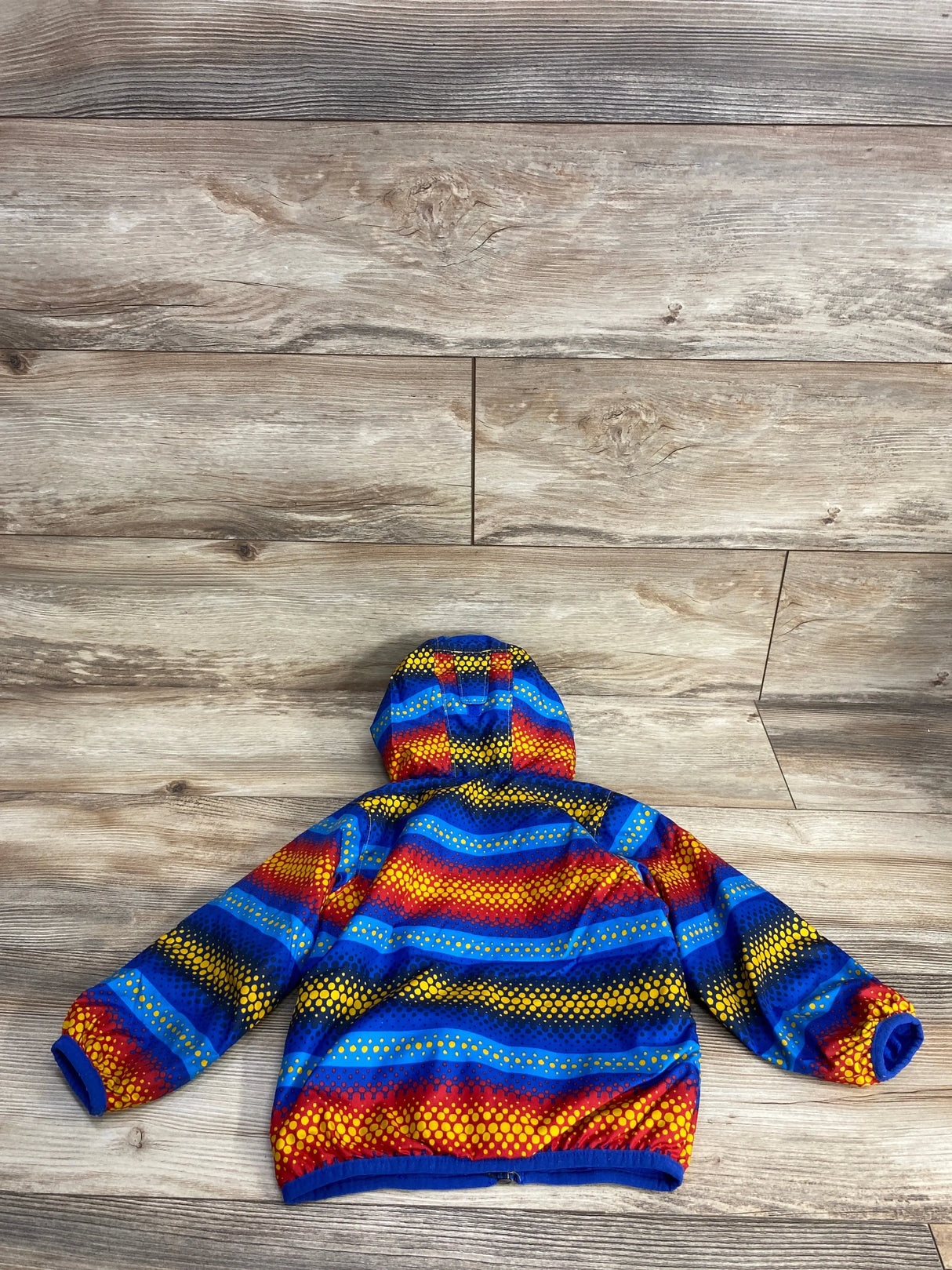Back view of Columbia hooded wind jacket with blue, red, and yellow dotted stripes, size 18-24 months, on wood background