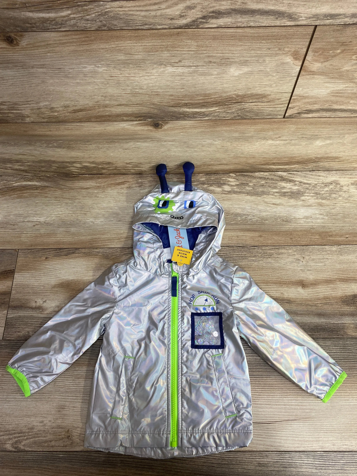 Silver kids' hooded rain jacket with green zipper and playful alien face on hood