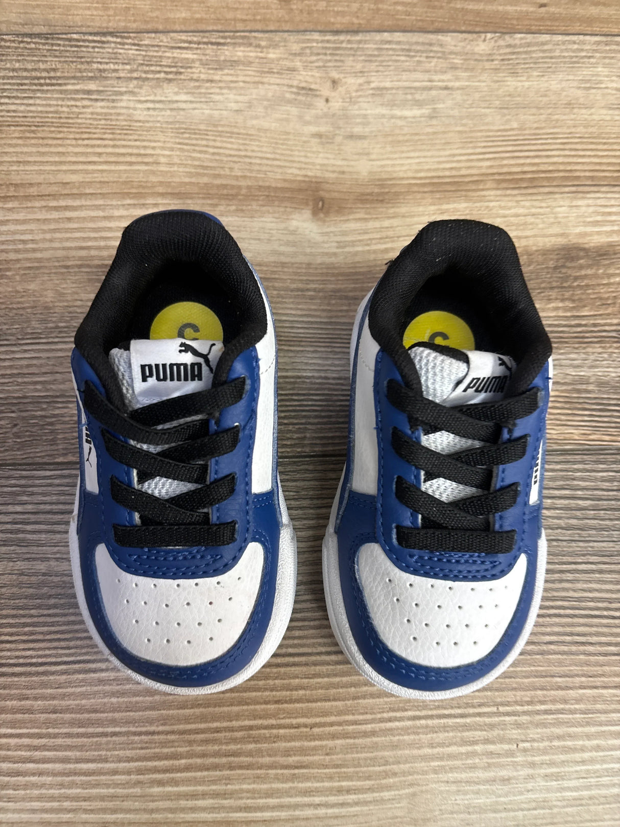 Blue and white Puma toddler sneakers with black laces on wood floor