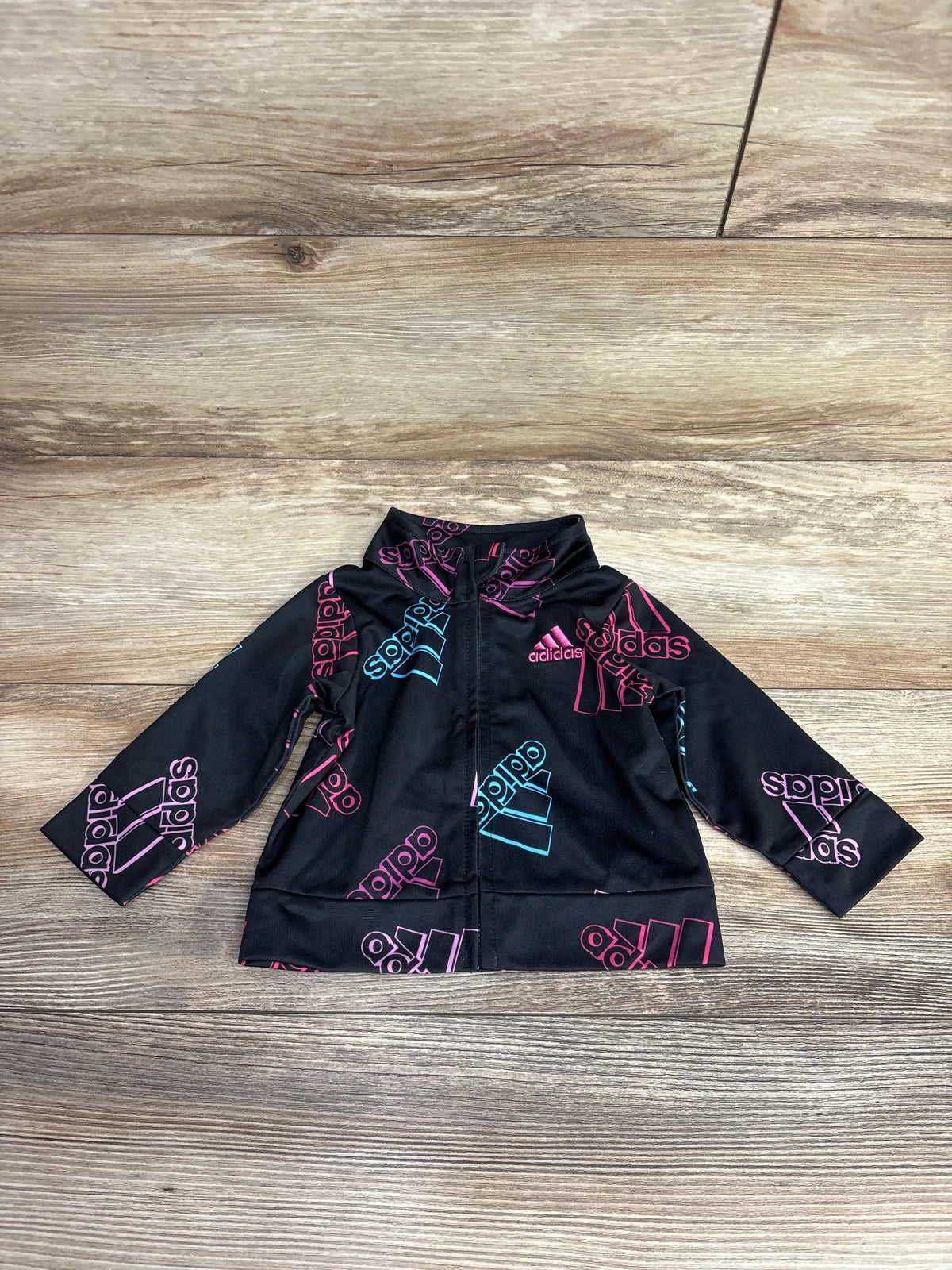 Black Adidas kids zip-up jacket with pink and blue logo patterns on wooden floor