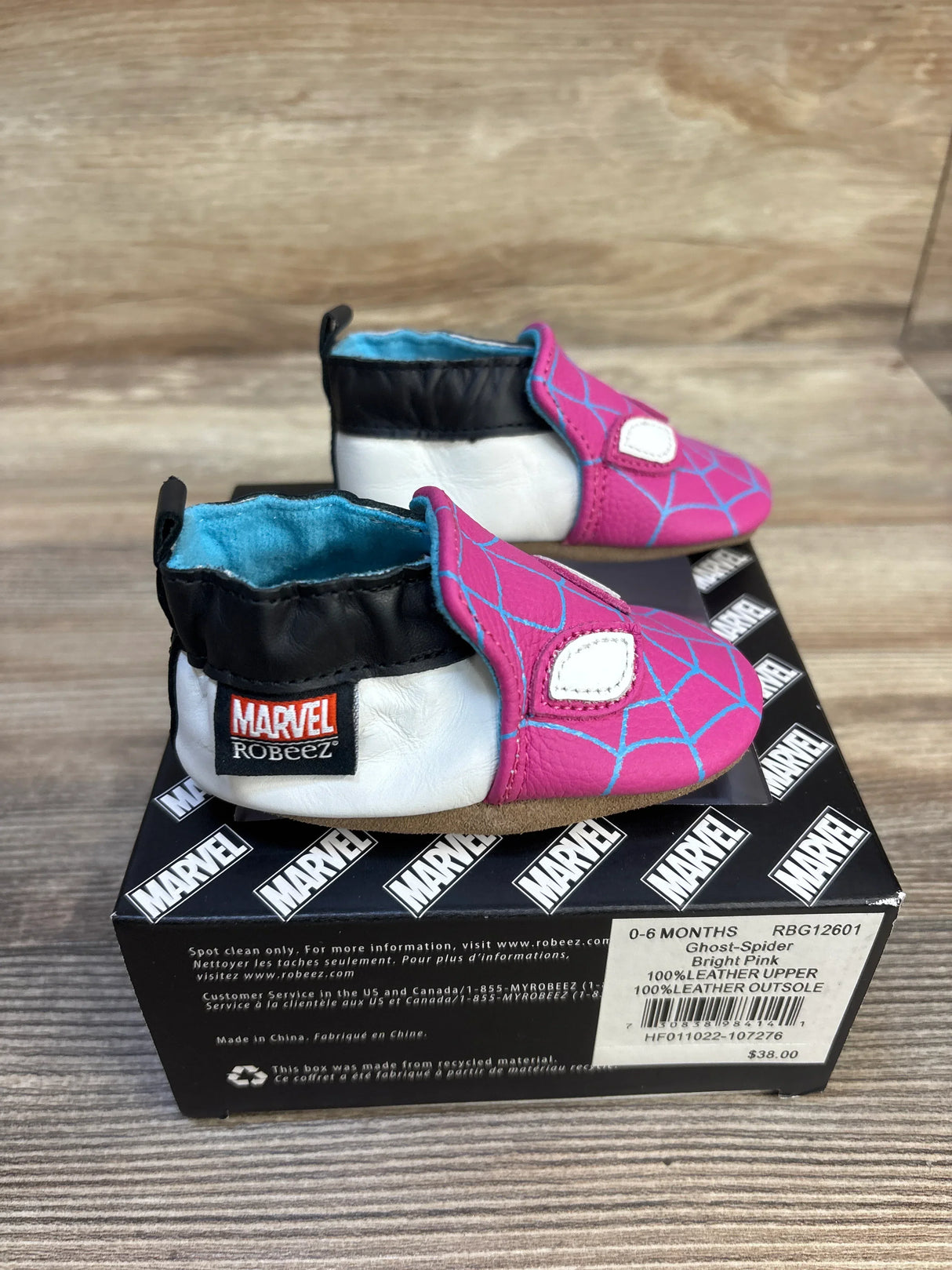 Three-quarter view of pink Robeez Ghost-Spider soft-sole shoes showing blue web design, white leather sides on Marvel box