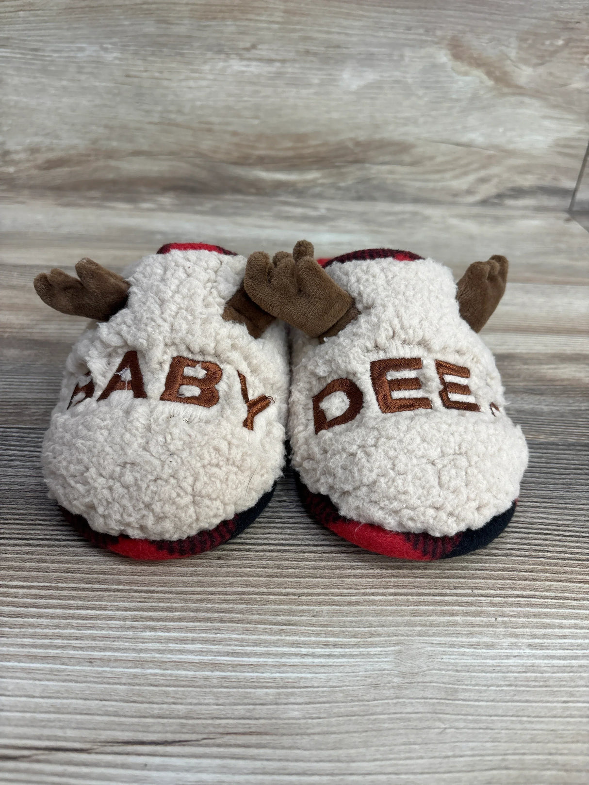 Plush baby slippers with 'BABY DEER' text and brown antler details on wood background