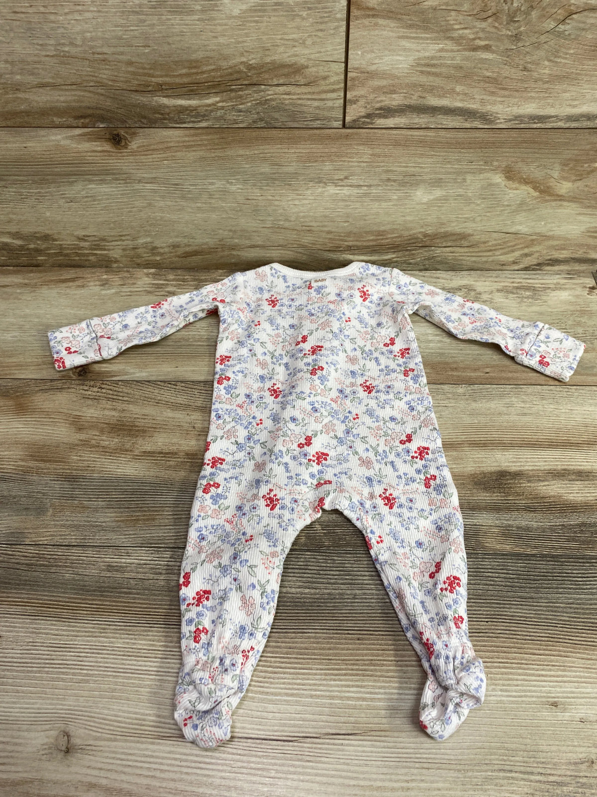 White organic cotton baby sleeper with a blue and red floral print on a wood background