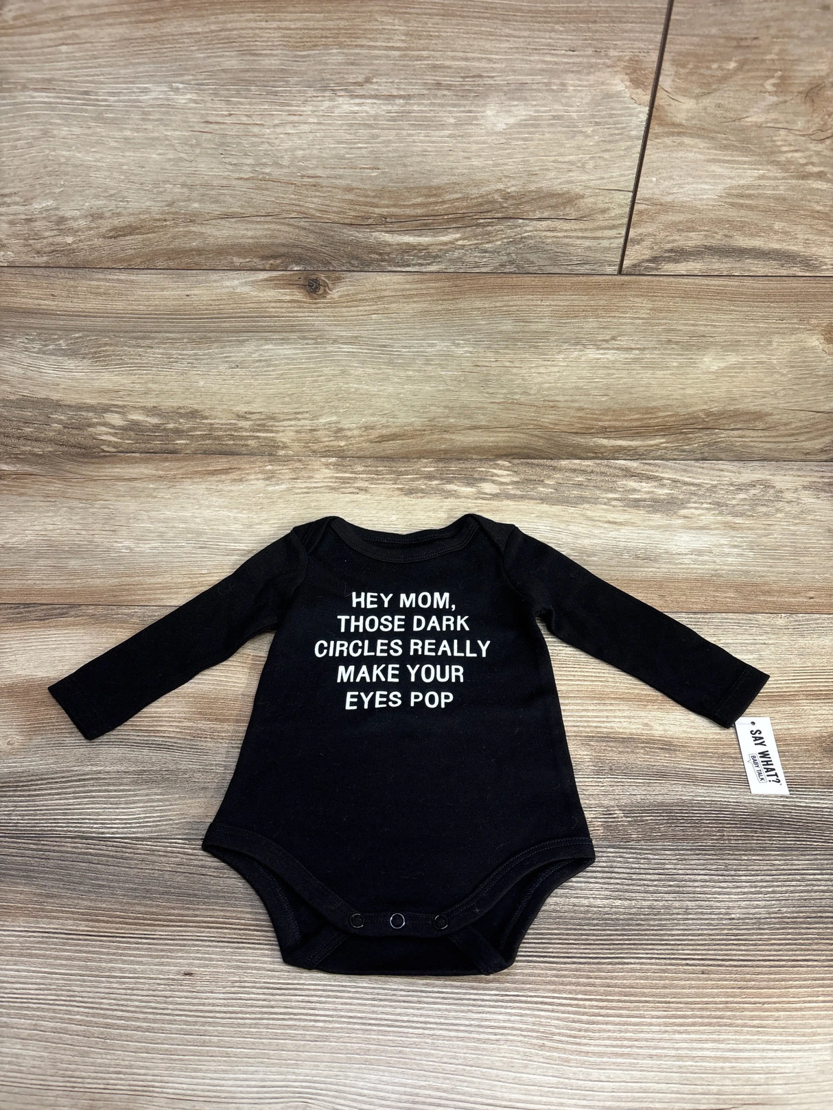 Black long sleeve baby bodysuit with funny text for moms, laid flat on wood background