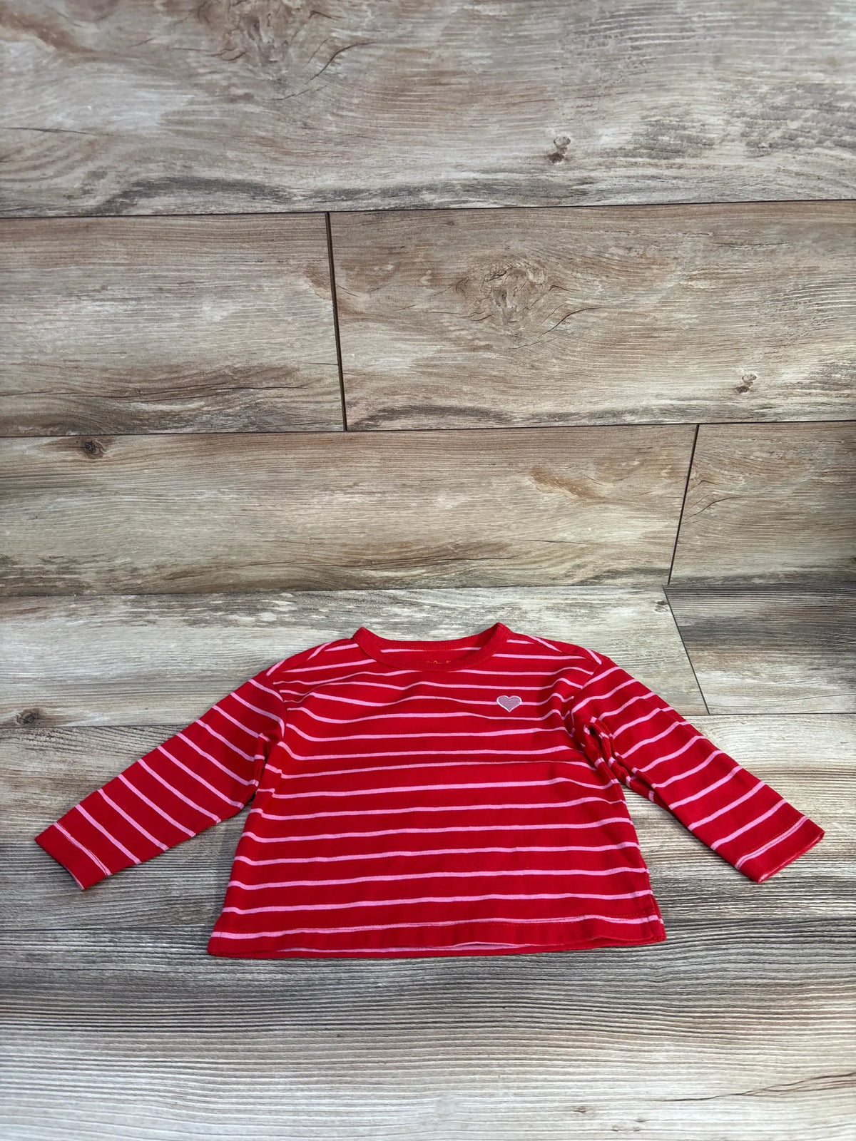 Front view of Cat & Jack red striped long sleeve shirt showcasing a small heart detail with a wood floor background