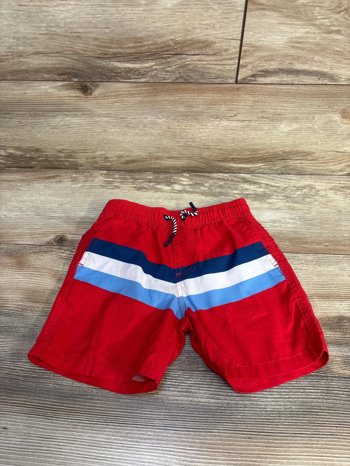Flat lay of Andy and Evan boys' red swim trunks size 4T with navy, white, and light blue stripes and drawstring on wood