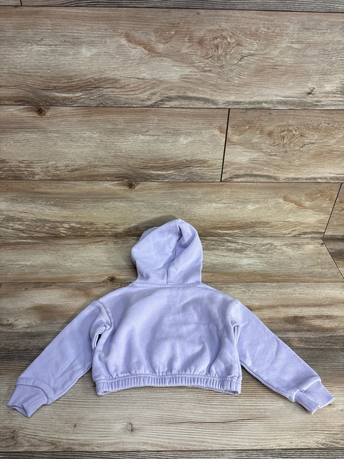 Back view of light purple cropped hoodie with long sleeves on wooden floor