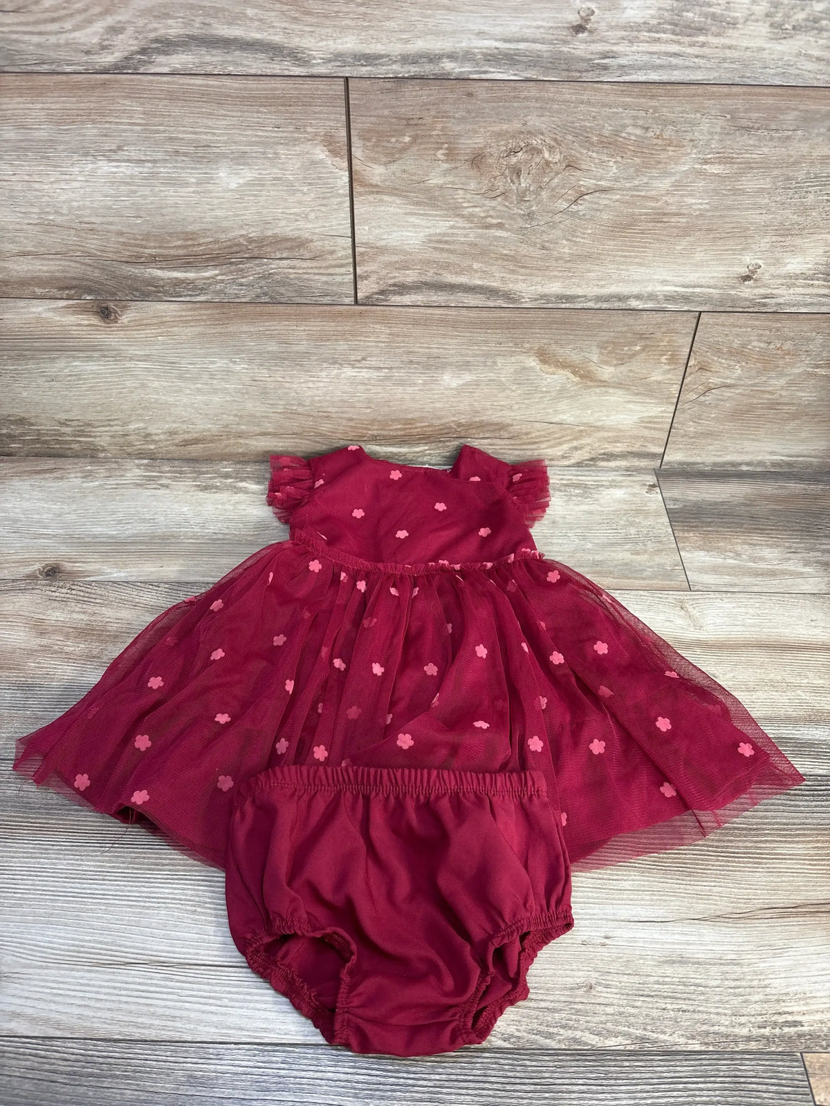 Flat lay of maroon tulle dress and matching bloomers showcasing sheer dotted skirt and elastic waist on wood floor background