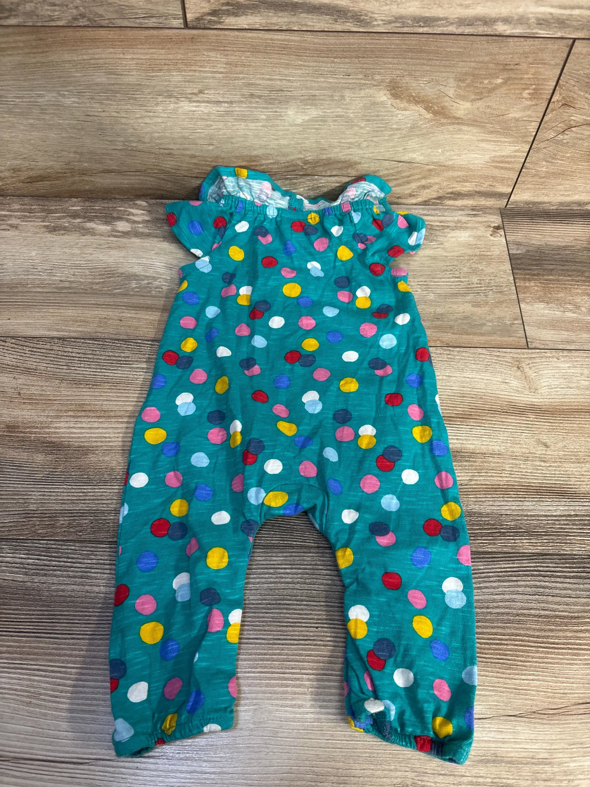 Front view of Frugi organic polka dot playsuit showcasing teal fabric and colorful polka-dot pattern on a wood floor