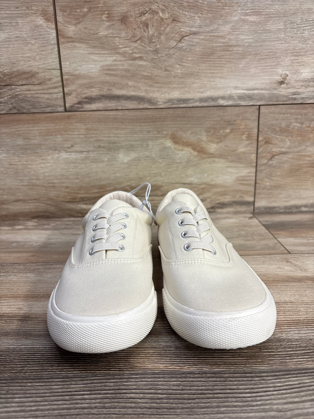 Front view of Cat & Jack cream canvas kids sneakers size 5Y with lace up front and white rubber soles on wood floor