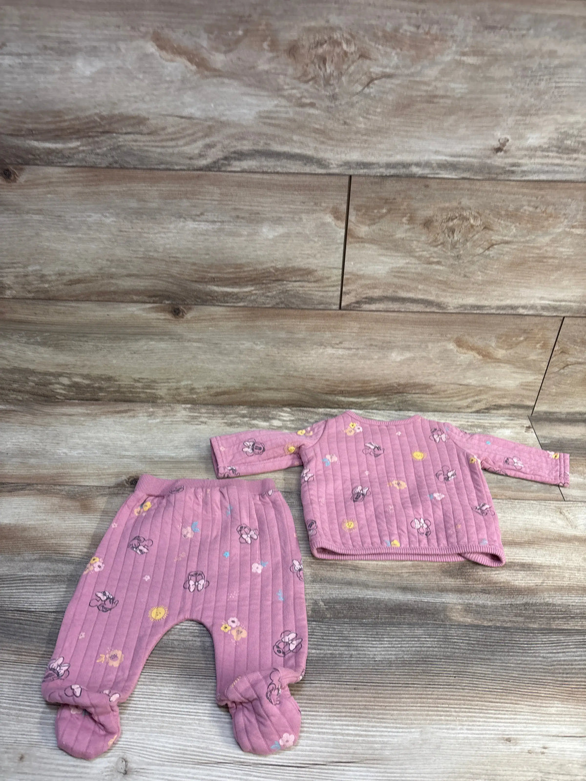 Flat-lay of pink Disney Minnie sweatshirt and footed pants showing quilted ribbed fabric and all-over print on wood
