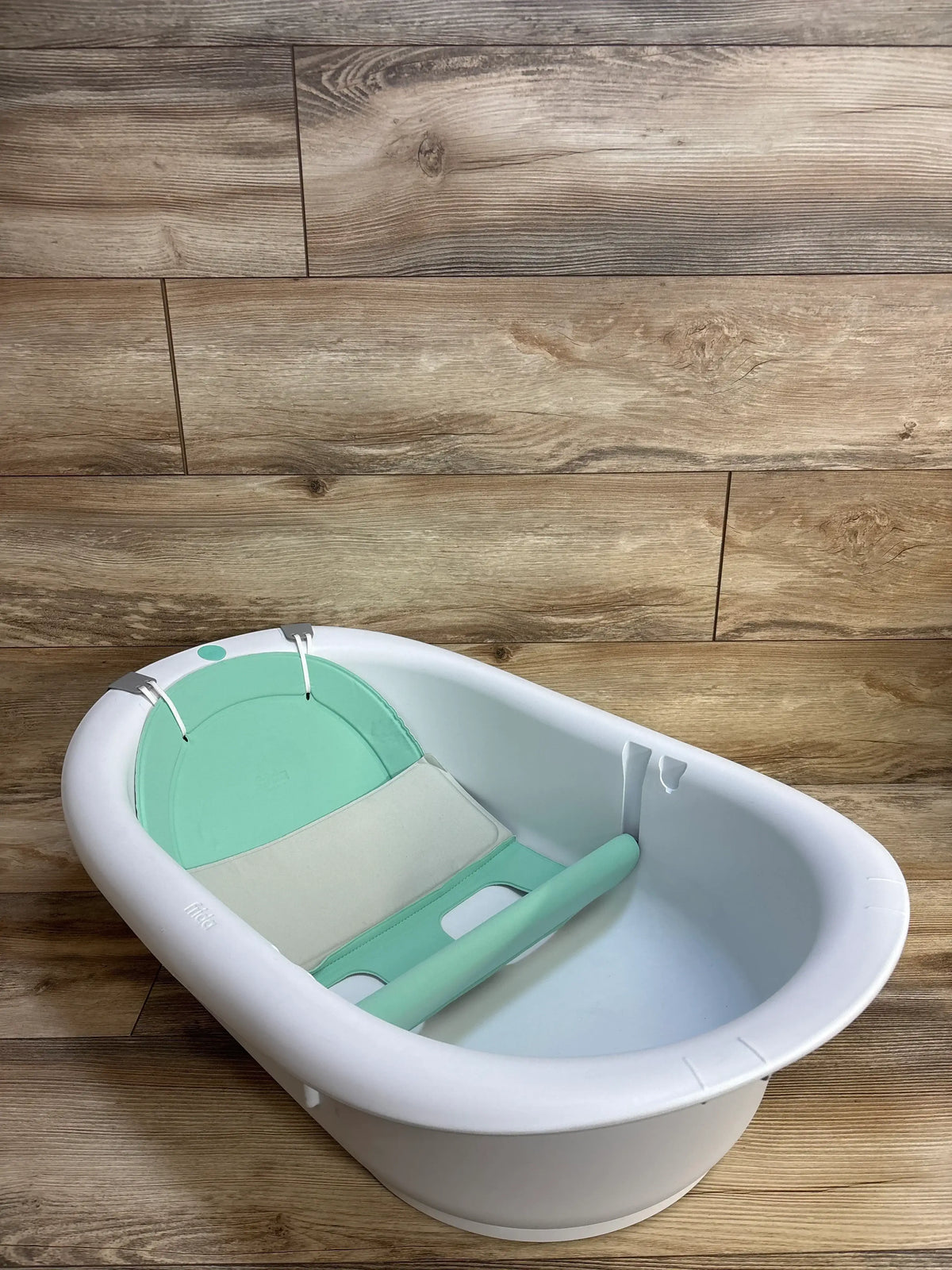 White baby bathtub with mint green support insert on wood floor, ideal for infant bath time