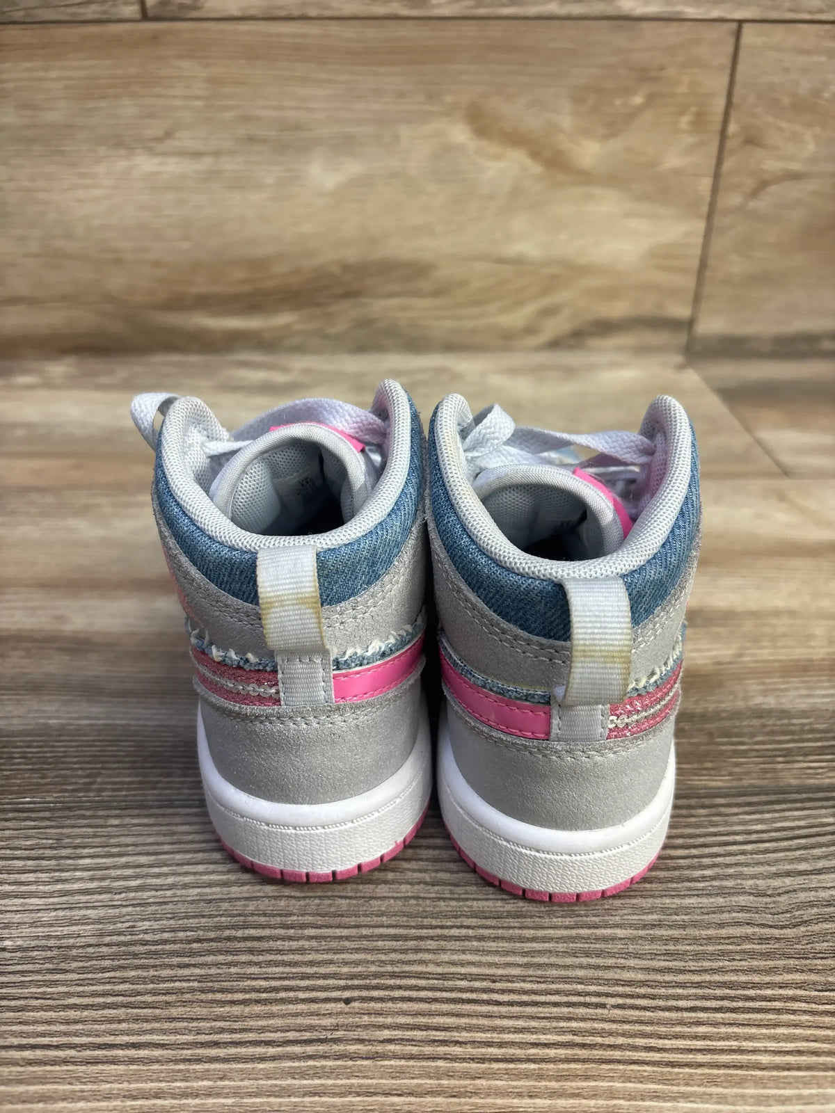 Rear view of Air Jordan 1 Mid SE PS toddler sneakers size 11C showing denim collar, pink stripe and white midsole on wood floor