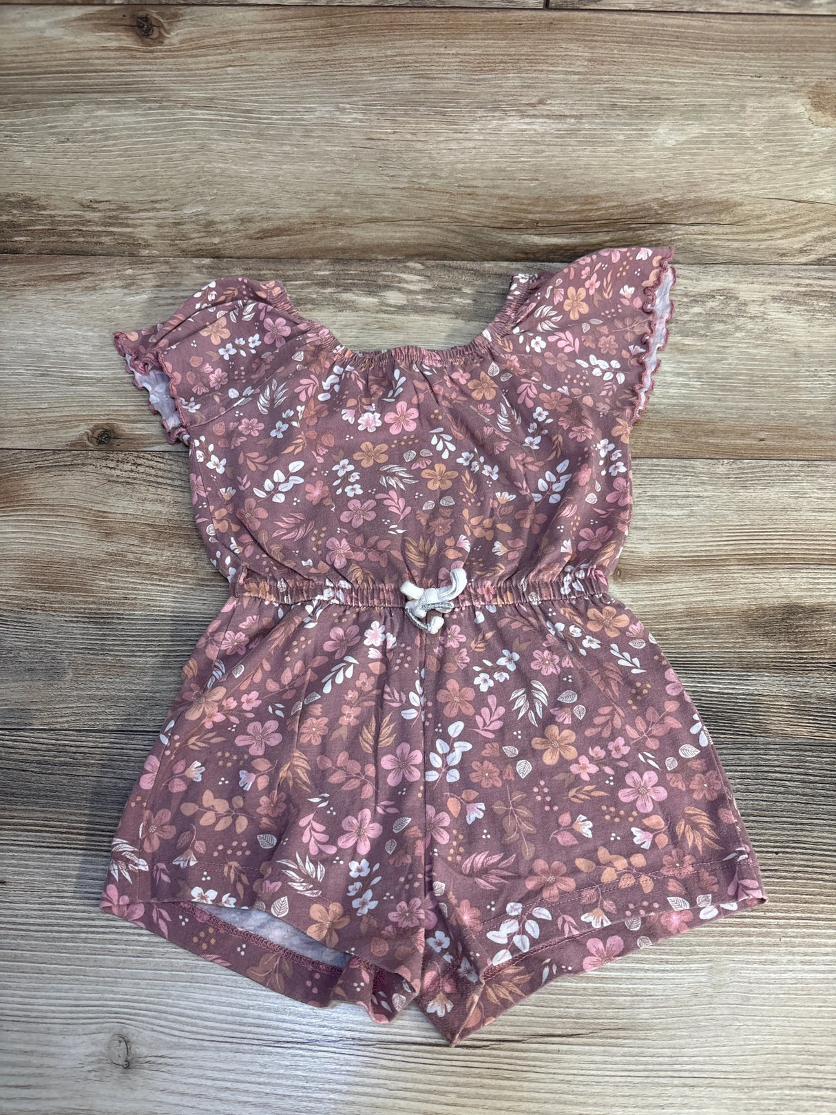 Floral baby romper with ruffled sleeves and drawstring waist, laid on wood floor