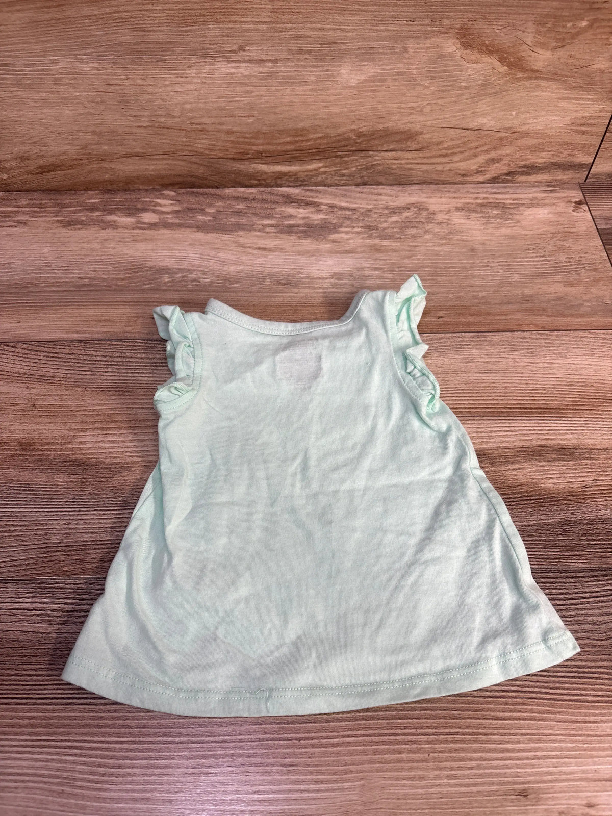 Back view of teal First Impressions butterfly tank top showcasing ruffled shoulder straps on a wood surface