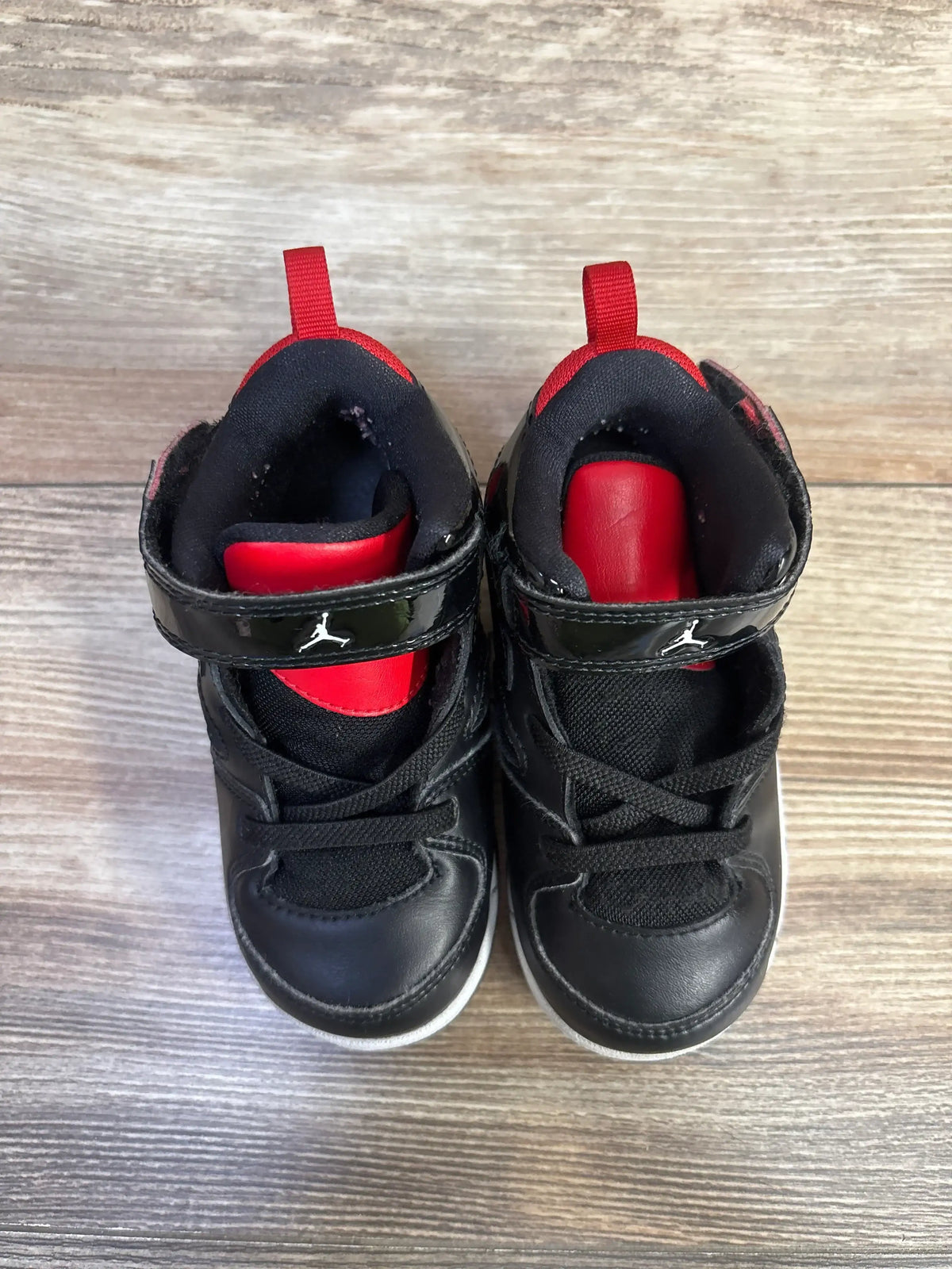 Top view of Air Jordan Flight Club 91 toddler sneakers, black leather with red tongues and velcro strap on wood floor