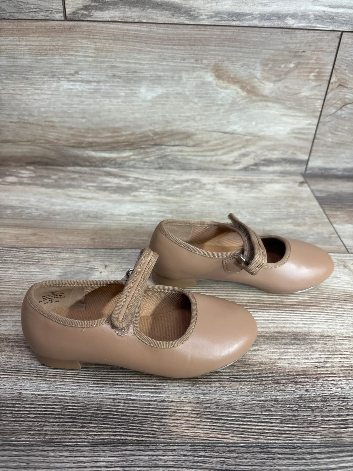 Angled top view of tan children's tap shoes (size 9C) showcasing Mary Jane strap and low heel on wood plank floor