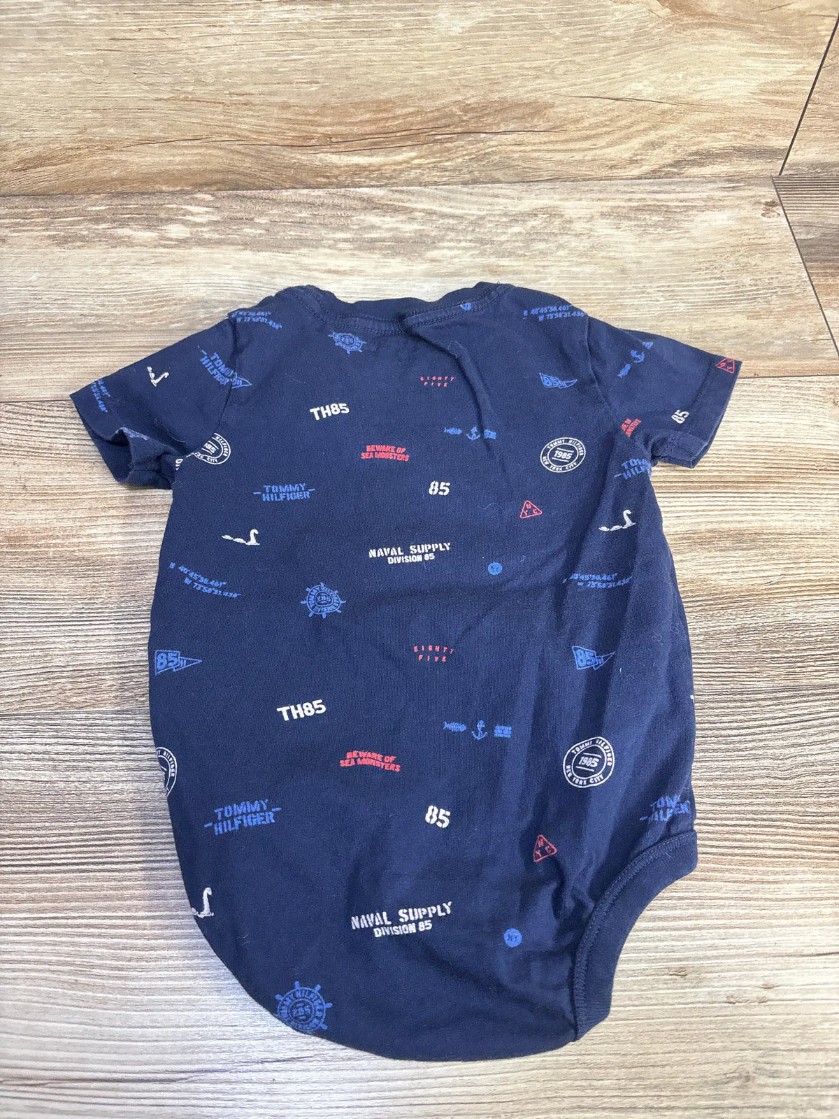 Front view of Tommy Hilfiger navy bodysuit showcasing an all-over nautical graphic print on a wood-look floor