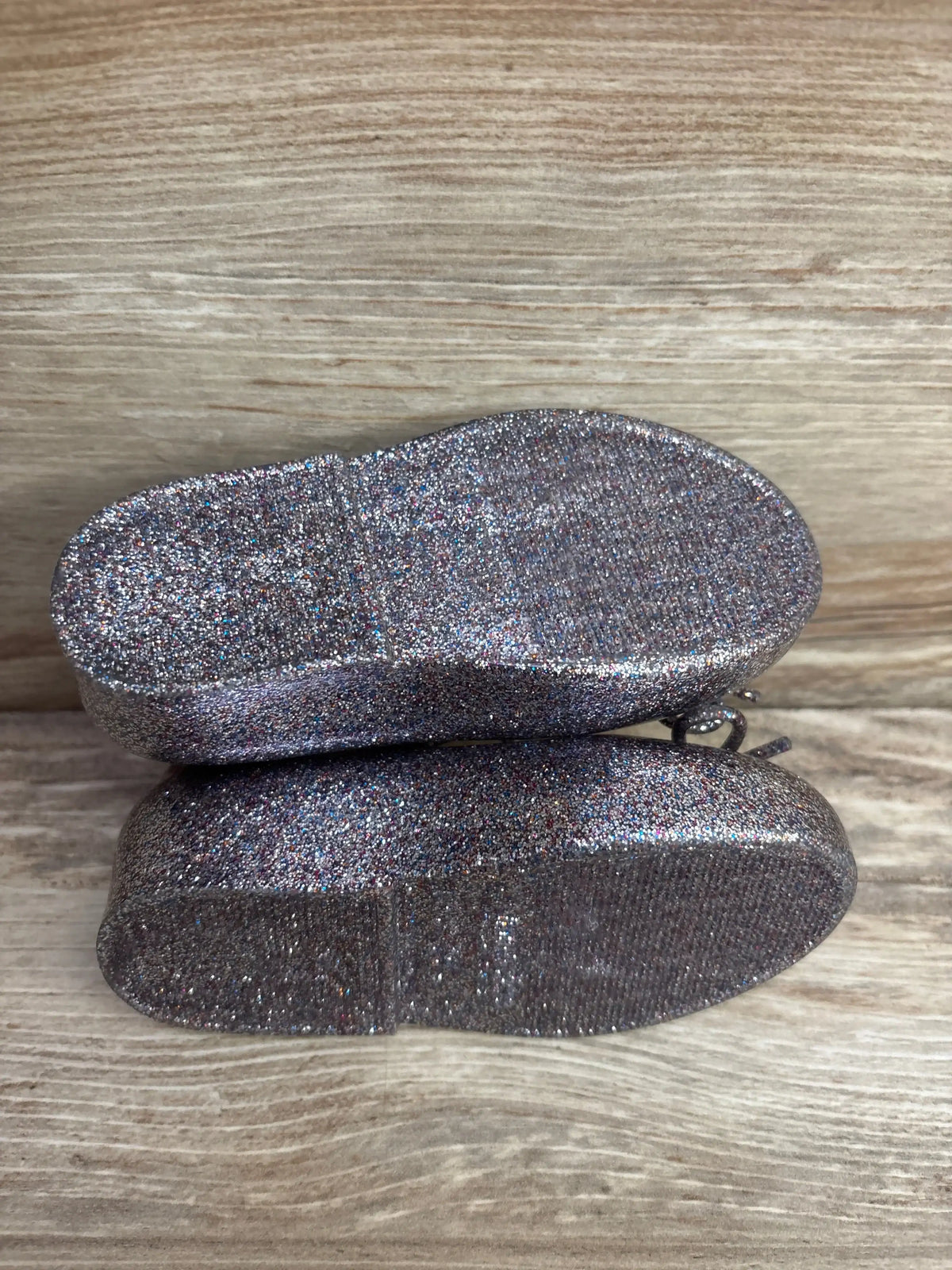Top view of Mini Melissa jelly flats, size 7C, with silver glitter finish and textured soles on wood background