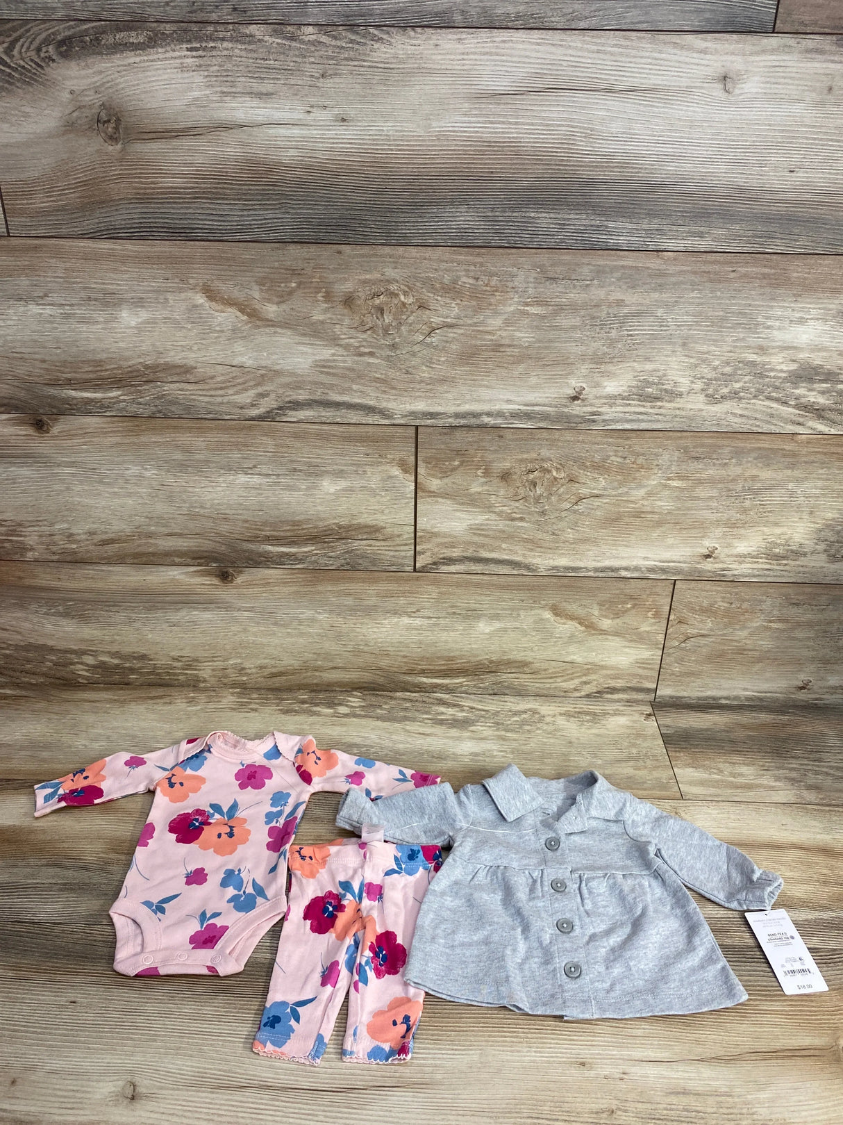 Baby girl floral bodysuit, matching pants, and gray button-up jacket set on wood background