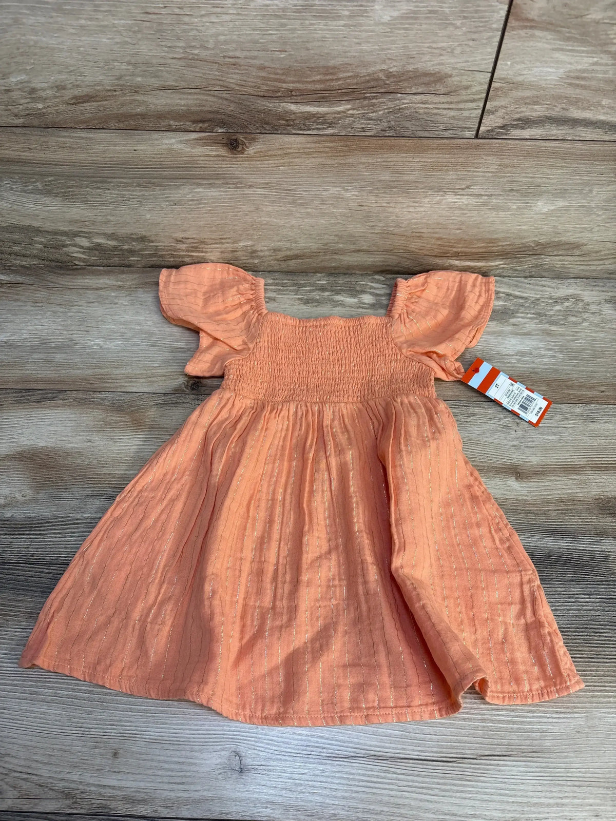 Peach baby dress with flutter sleeves and shimmer stripes, size 2T, laid on wood floor