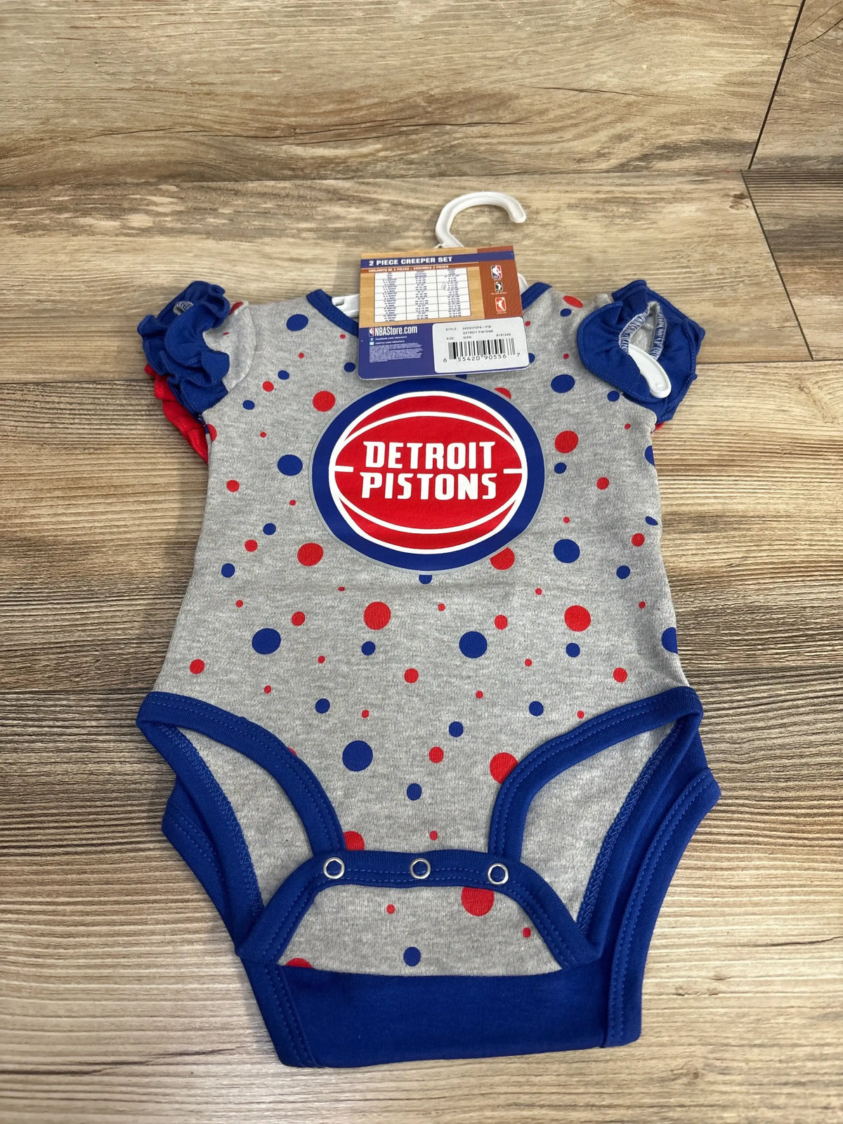 Detroit Pistons baby onesie, grey with blue and red polka dots, ruffled sleeves, on wood floor