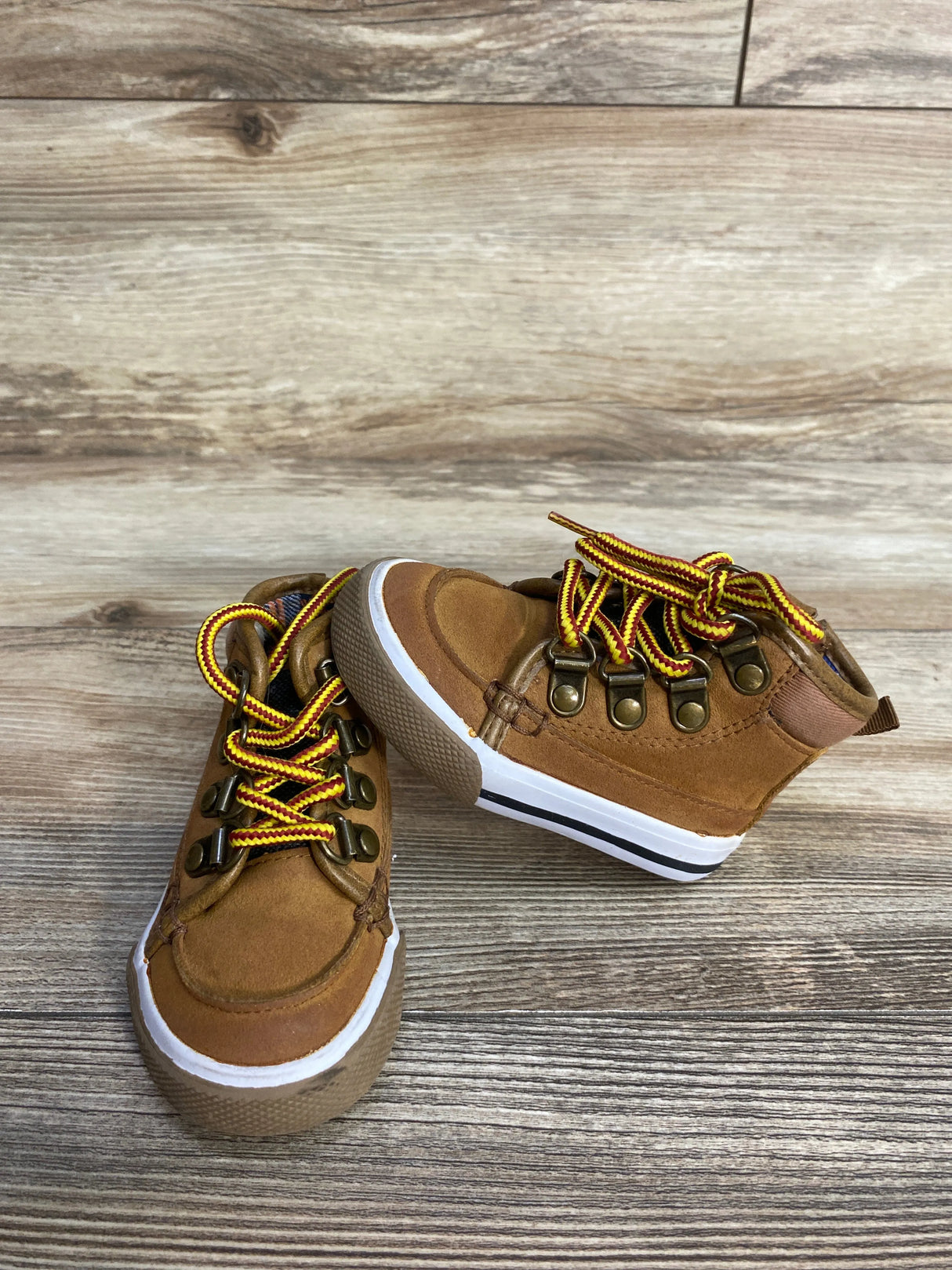Brown toddler hiking boots with yellow laces on wood floor background