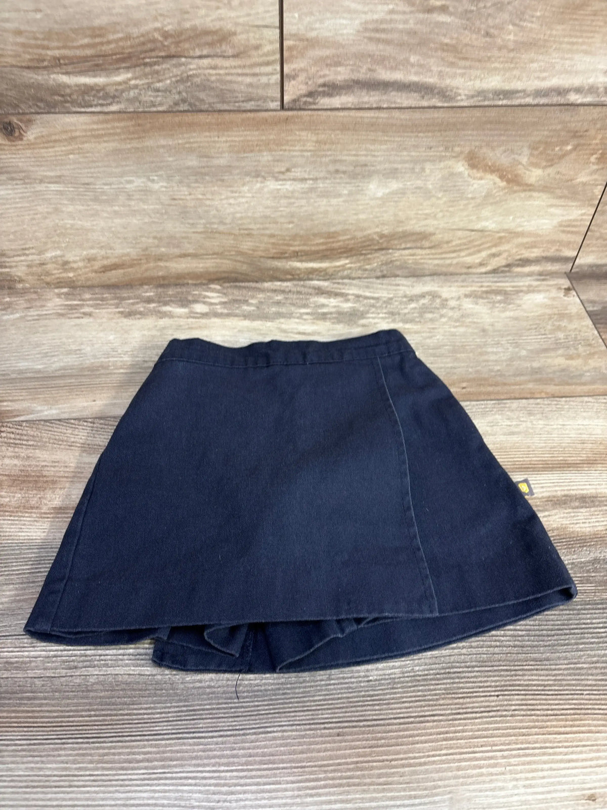 Top-down view of navy Dennis uniform skort showing A-line shape and built-in shorts on wood plank background
