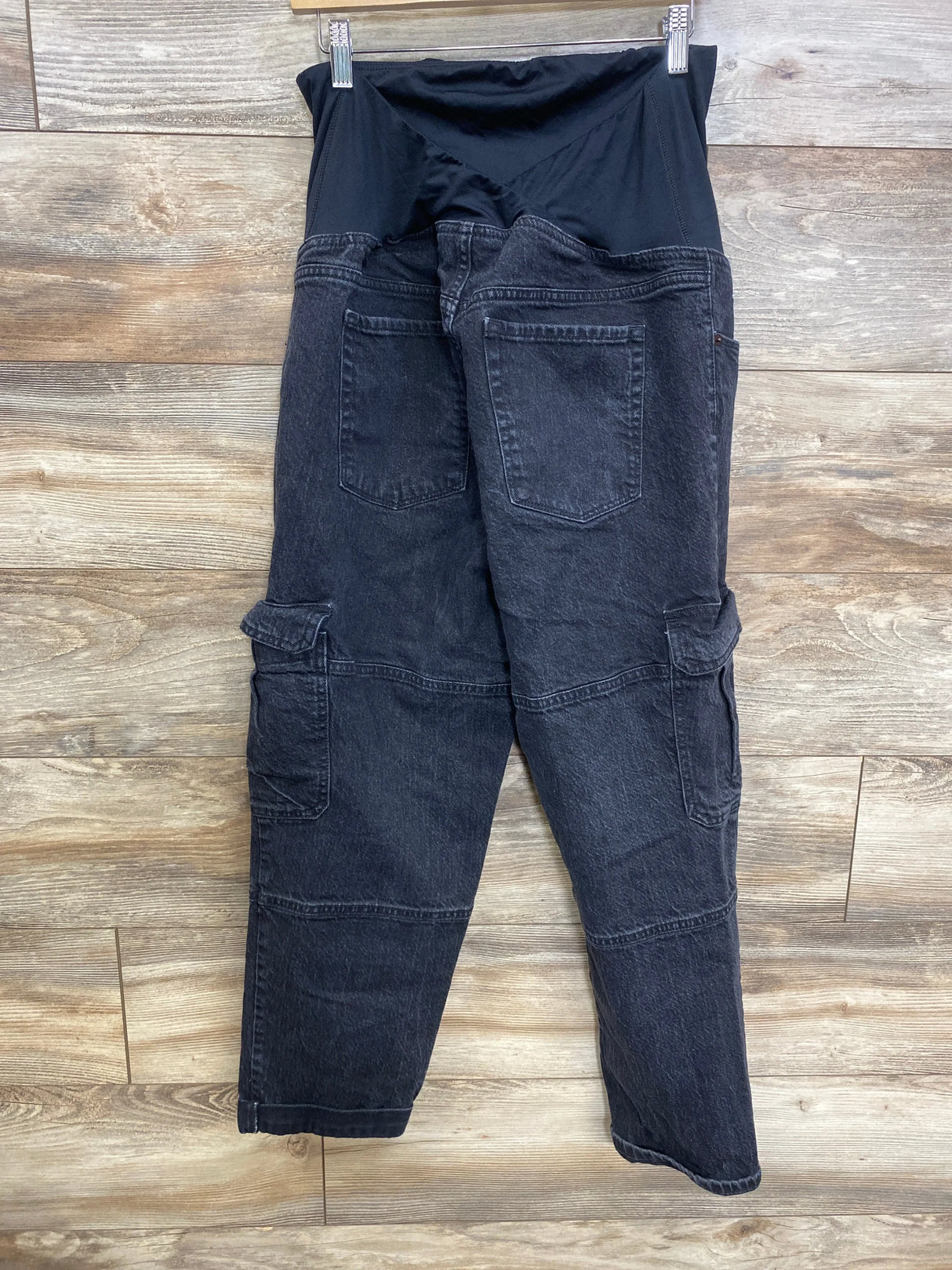 Back of black Isabel maternity 90s straight cargo jeans with elastic belly panel and cargo pockets on wood background